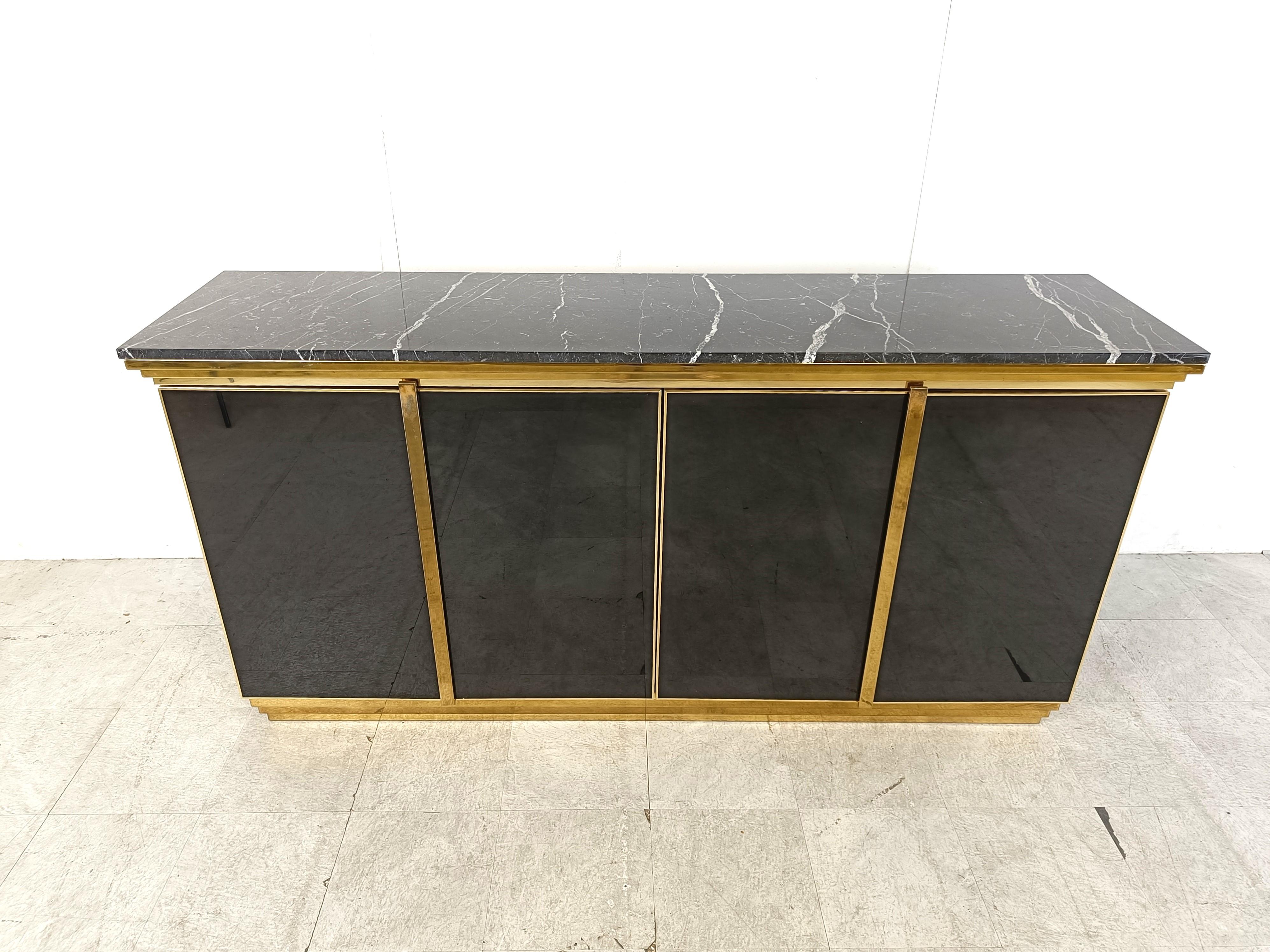Luxurious seventies glamour sideboard in the manner of Maison Jansen consisting of black glass panels, brass hardware and a black marble top.

The use of different high quality materials makes this piece a real eye catcher.

It also provides a lot