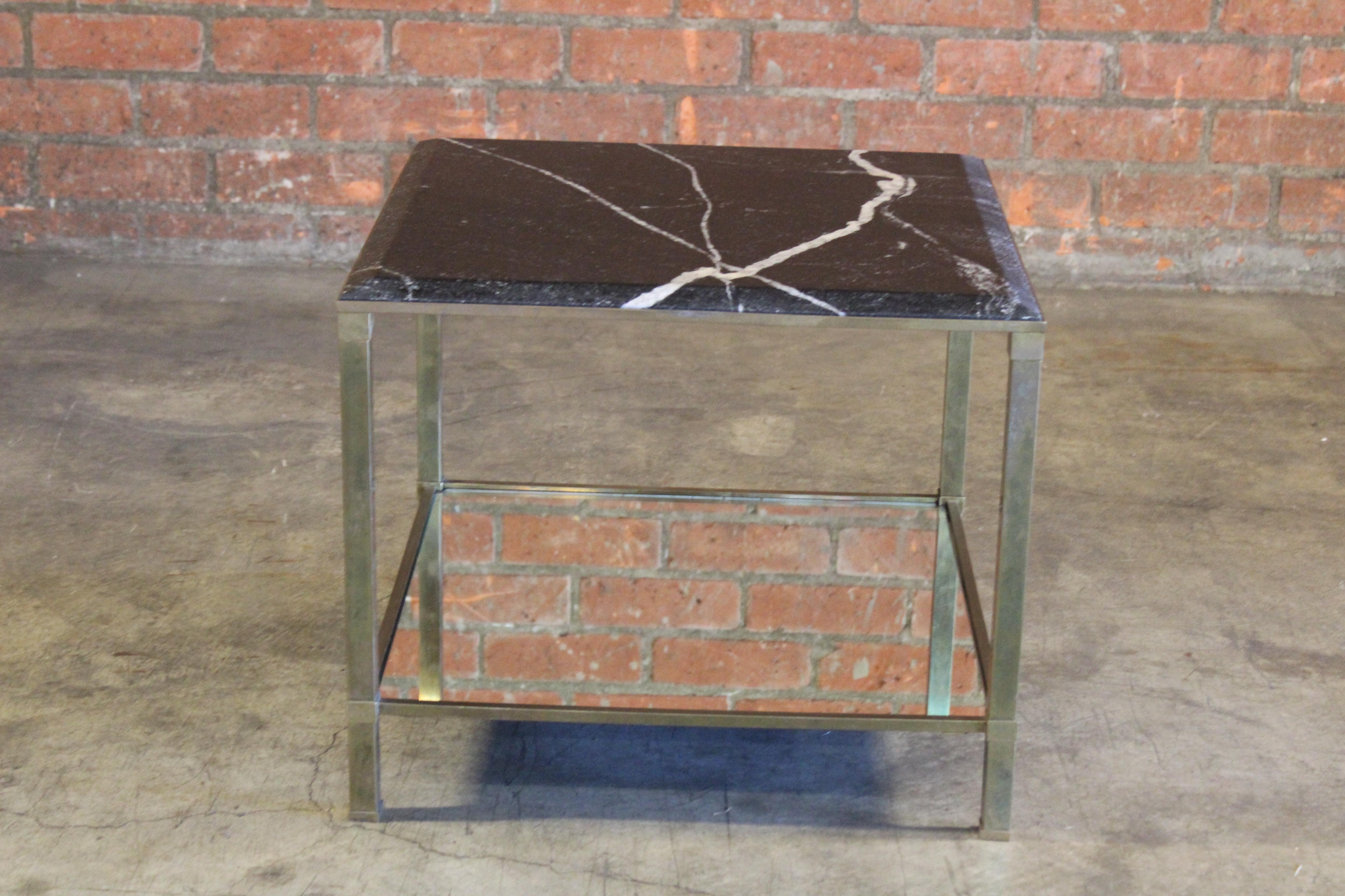 A vintage brass end table attributed to Maison Jansen. Features a black marble top with beveled detailing on top with white veining and a mirror shelf. In overall wonderful condition with patina to the brass.