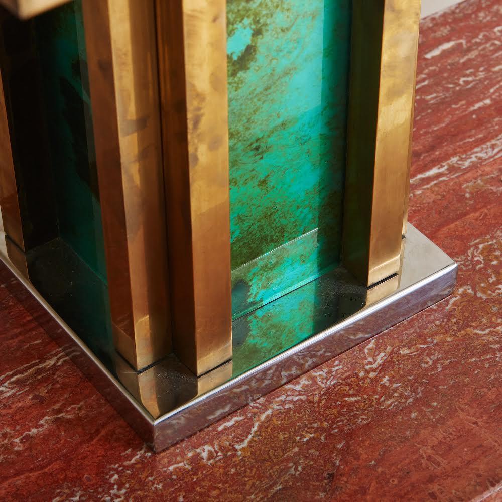 A Mid Century Italian table lamp designed by Romeo Rega. The lamp features an architectural base constructed with patinated brass and glass with a captivating green marbled effect. It has a square chrome platform and retains the original large scale