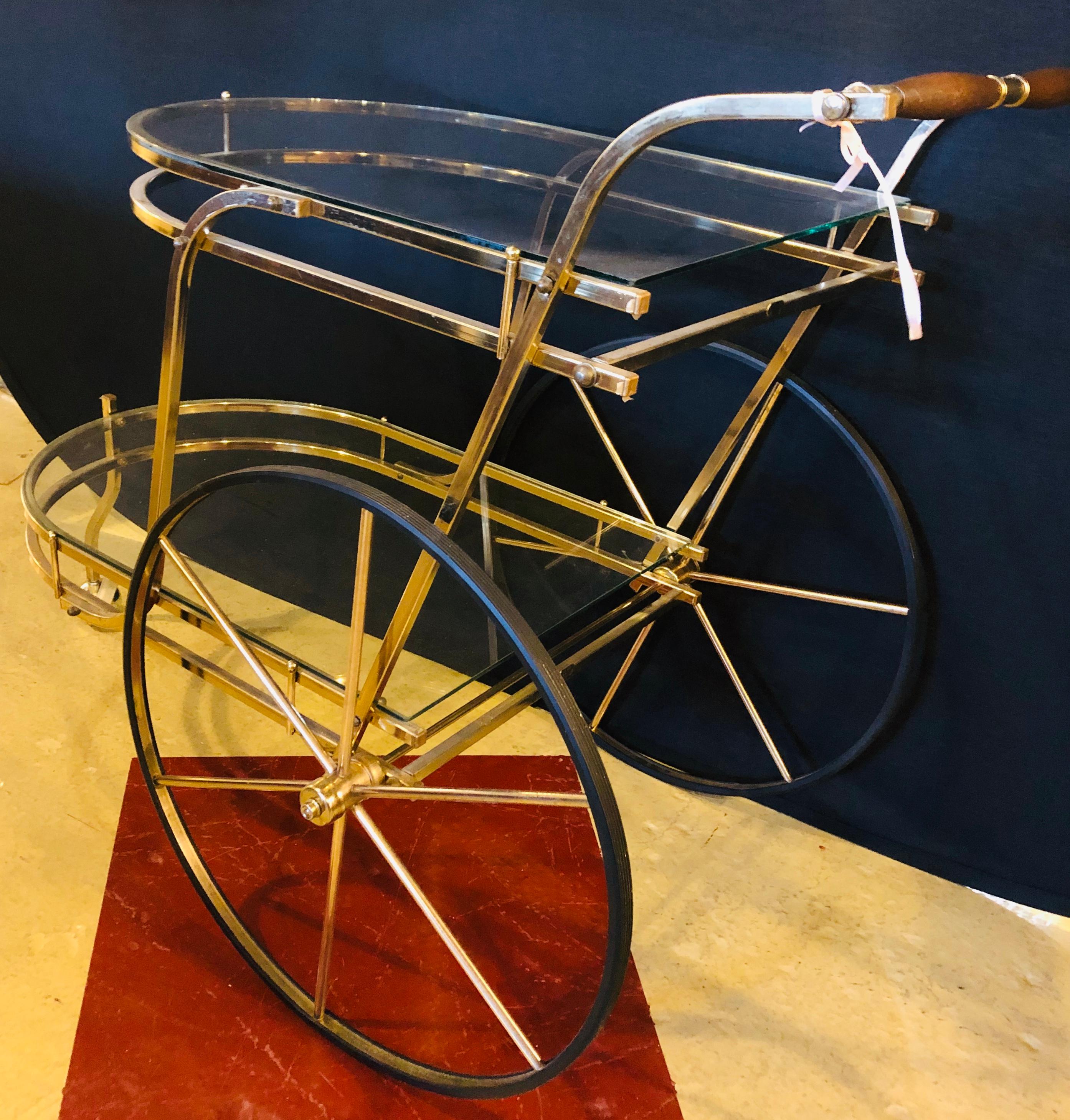 Brass Mid-Century Modern tea wagon or serving cart having two glass shelves with small ball caster in the front and two large decorative spoked wheels in the rear.