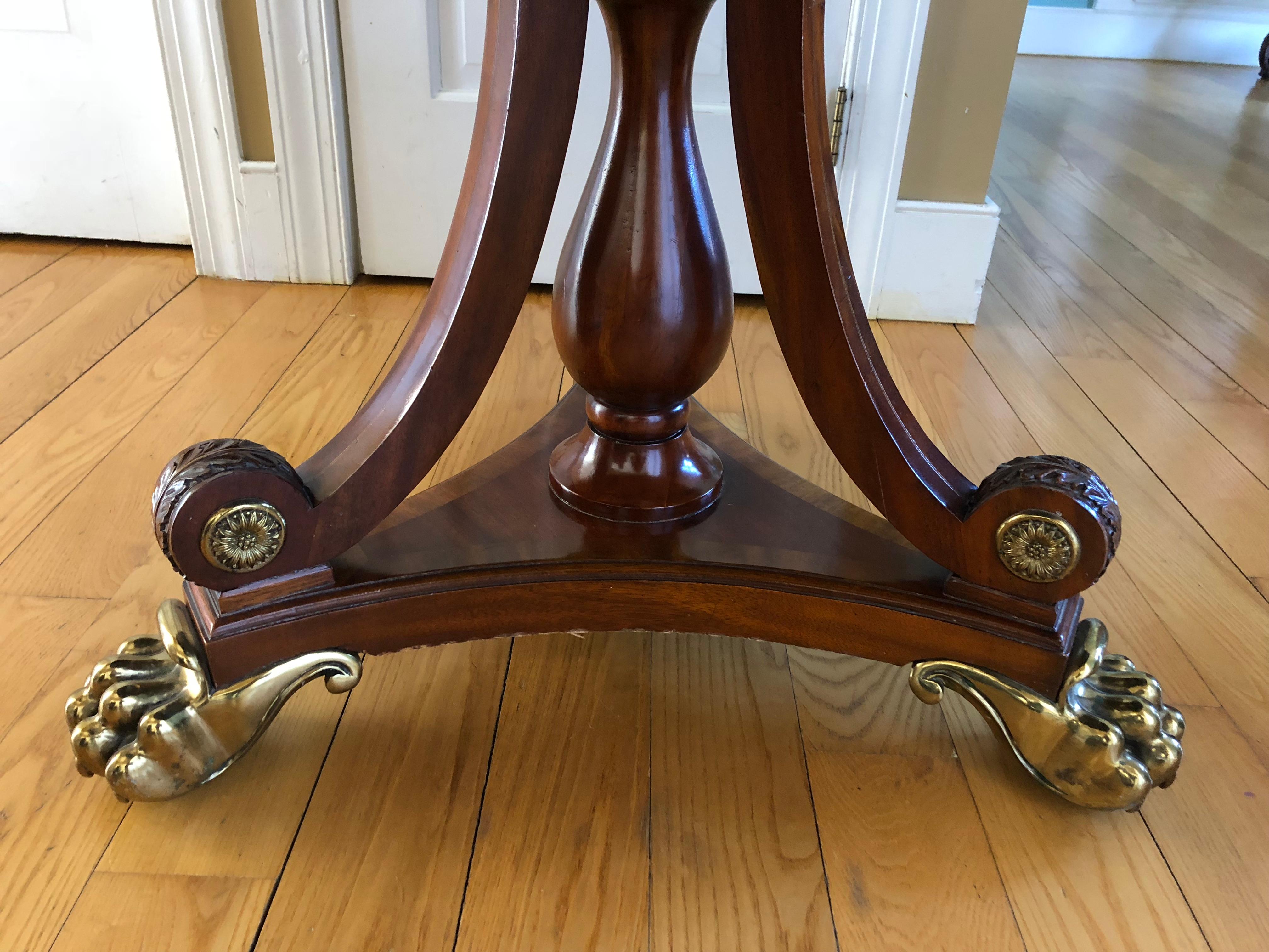 Maitland Smith brass-mounted mahogany and leather round drum or centre hall table. Regency style with tooled leather top and frieze. Having 3 functional drawers, metal embellishments and claw feet.
 