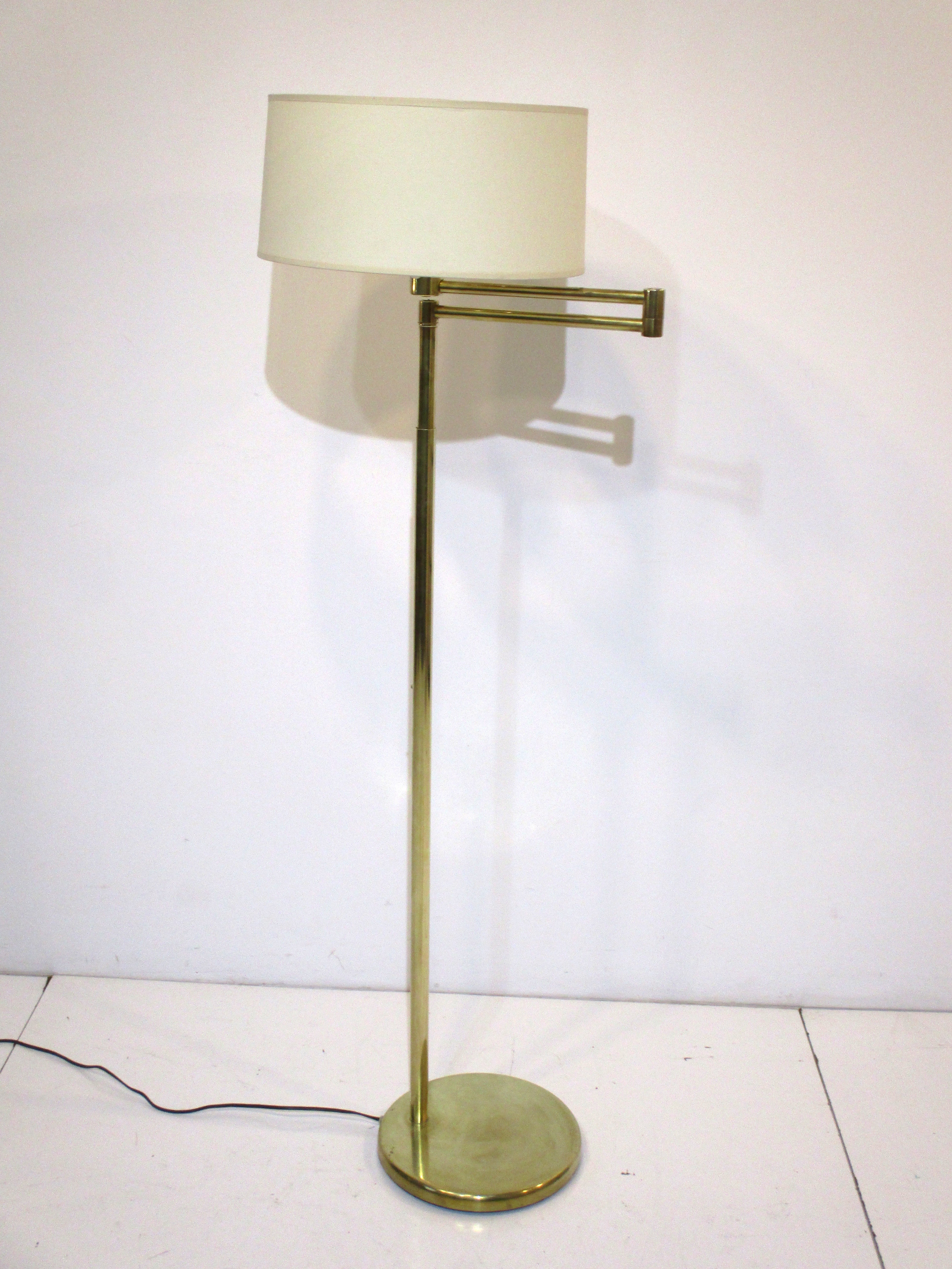 A very nice brass swing arm floor lamp topped with the original milk glass defusser and cream colored round linen shade . Manufactured by the Nessen Lighting Company NY known for their high quality and superior materials this lamp is a design icon