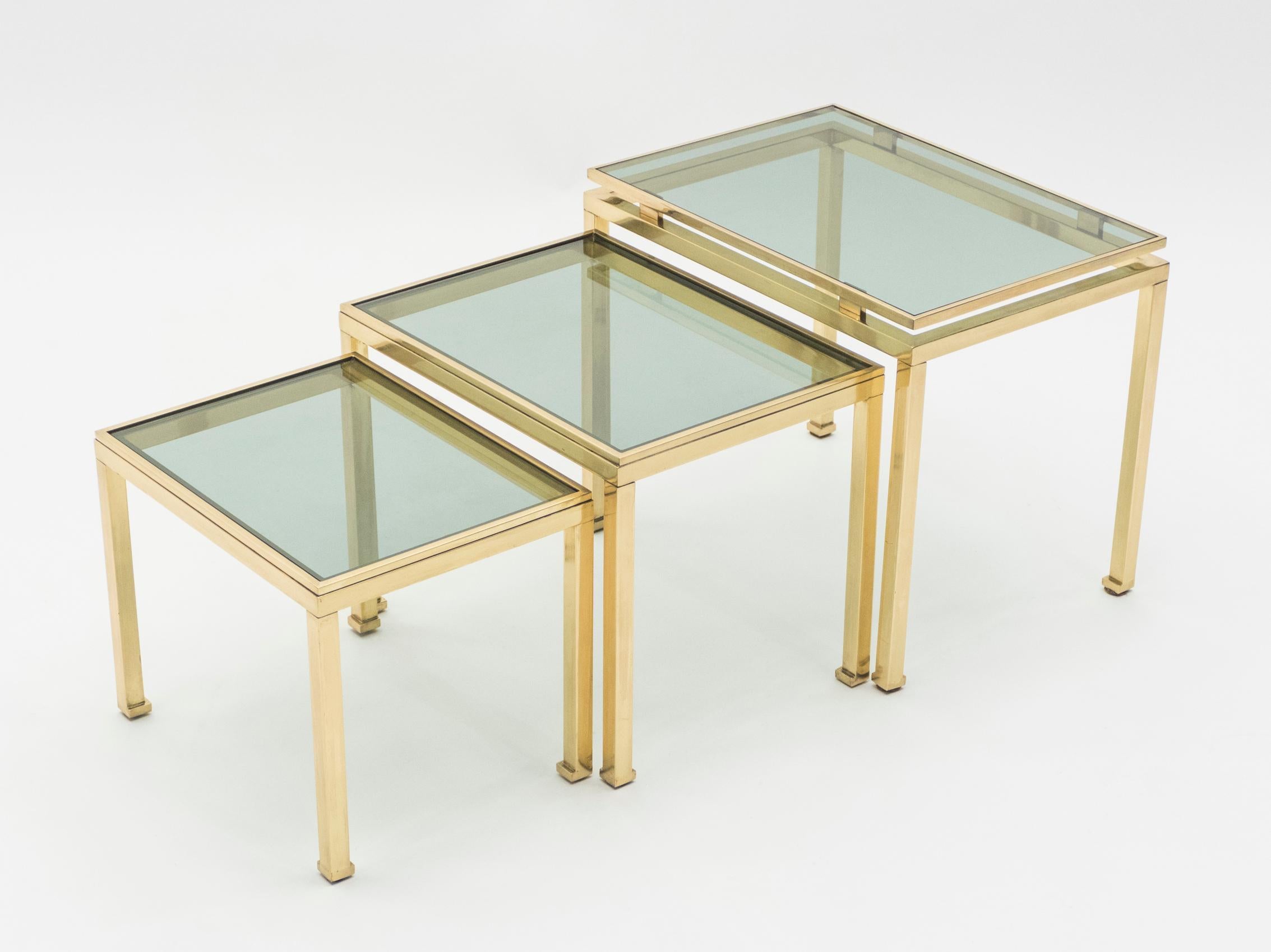 Simple lines point to this nesting tables midcentury roots. Designed by Guy Lefevre for Maison Jansen, it features silky brass legs and green smoked glass tops. Its symmetry, elevated glass, and strong architectural design combine to create a subtle