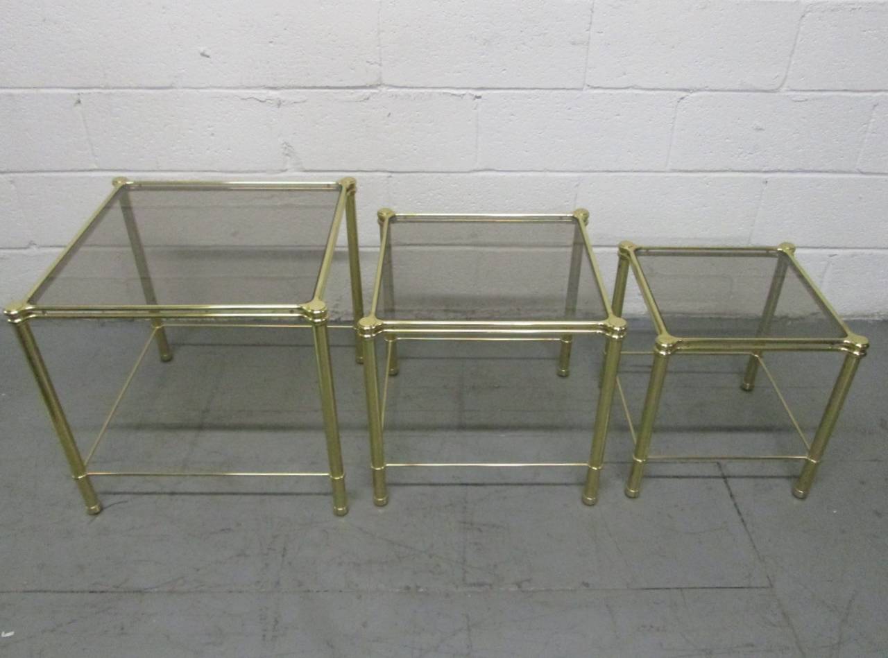 Nesting tables with a decorative brass frame and smoked glass tops.
Larger tables measures: 19.25