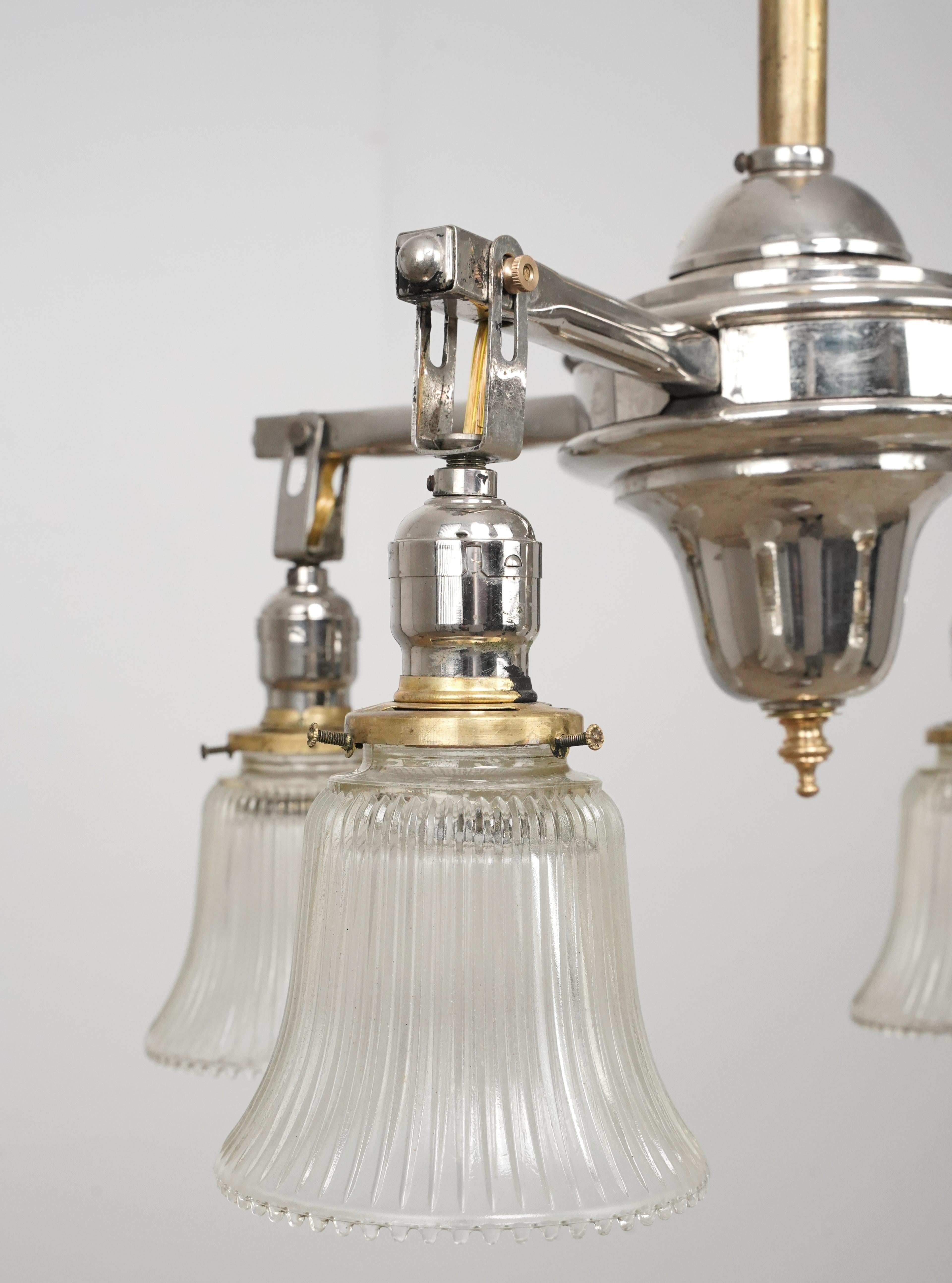Traditional style chandelier with four arms, with clear glass shades and a mixed brass and nickel finish pole. This requires four standard Edison style medium base bulbs. This light is cleaned and restored and ready to ship. Good condition with