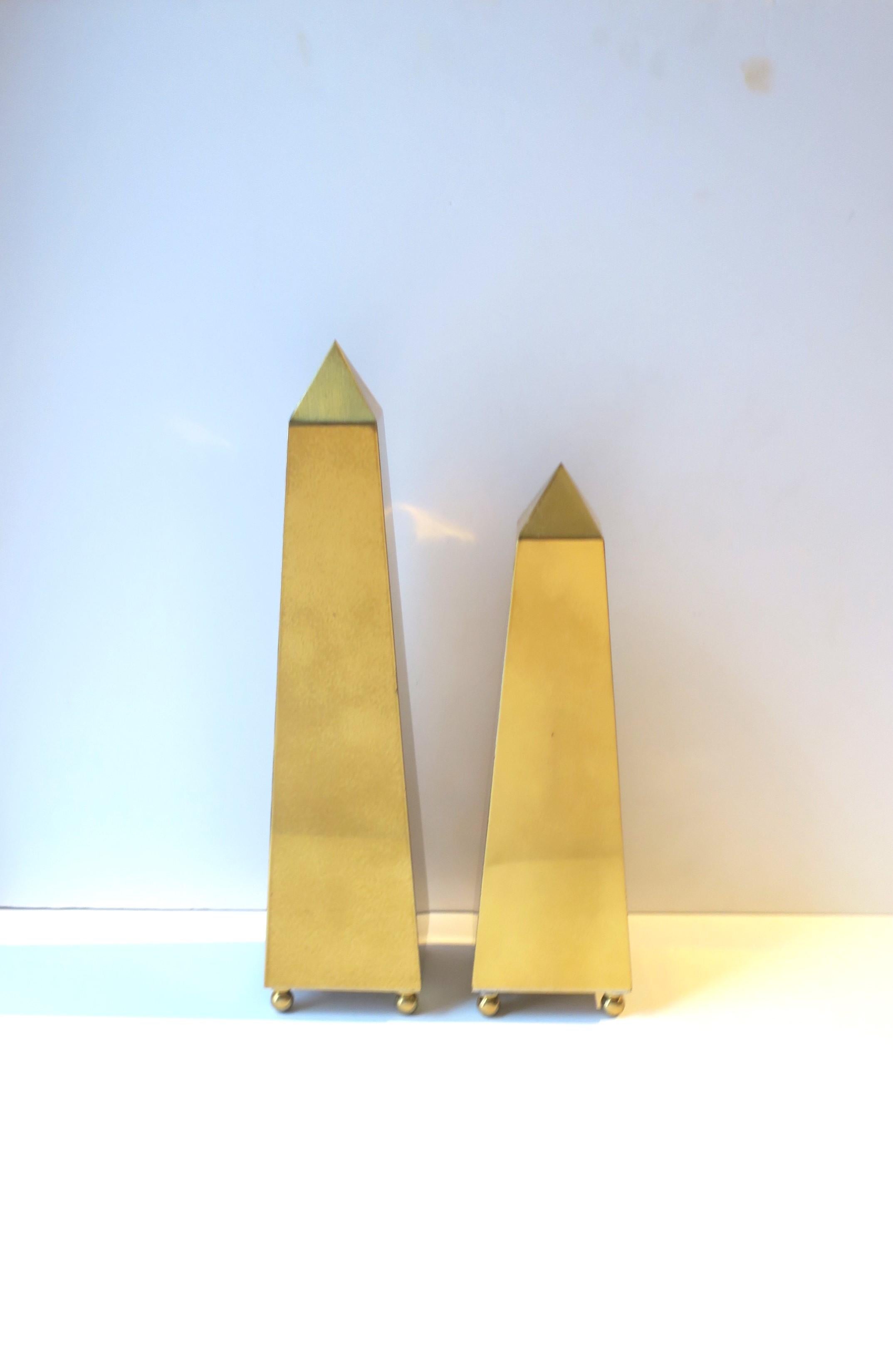 A pair/set of brass Obelisks with ball feet, in the Modern style, circa late 20th century. Pair have a clear lacquer overlay; brass will maintain its shine. A great set of decorative objects for a mantle, credenza, cocktail table, etc. 

Dimensions: