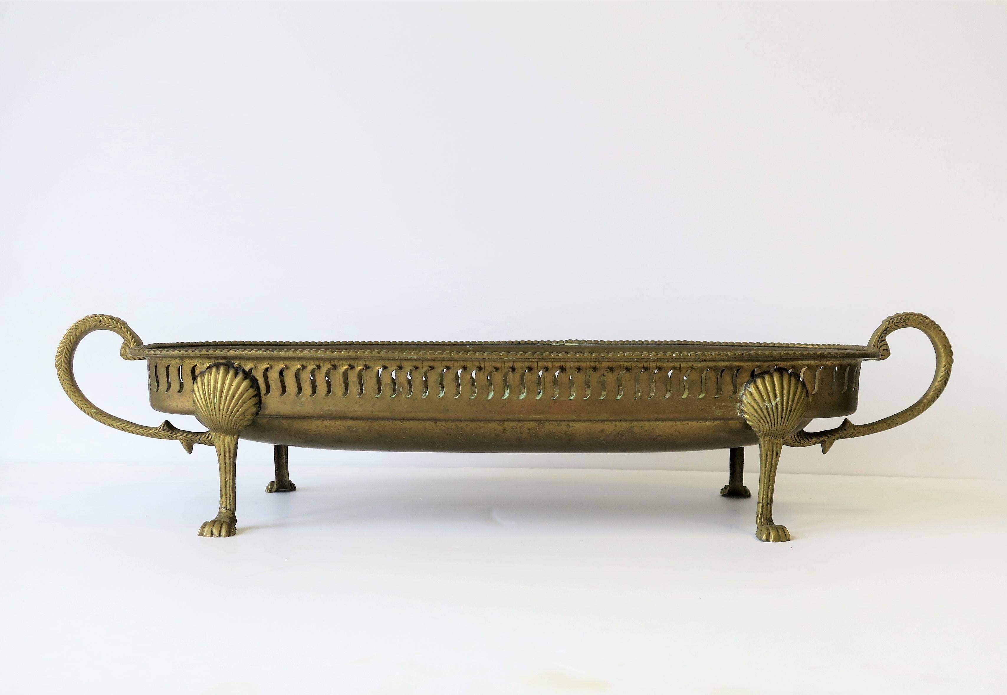 A beautiful brass footed oblong centerpiece, or vide-poche (catch-all) vessel, circa early 20th Century. Legs have oyster shell and paw feet detail in the Regency style. 

Measures: 7 in. D x 20 in. W x 4 in. H

Medium sized seashell featured in