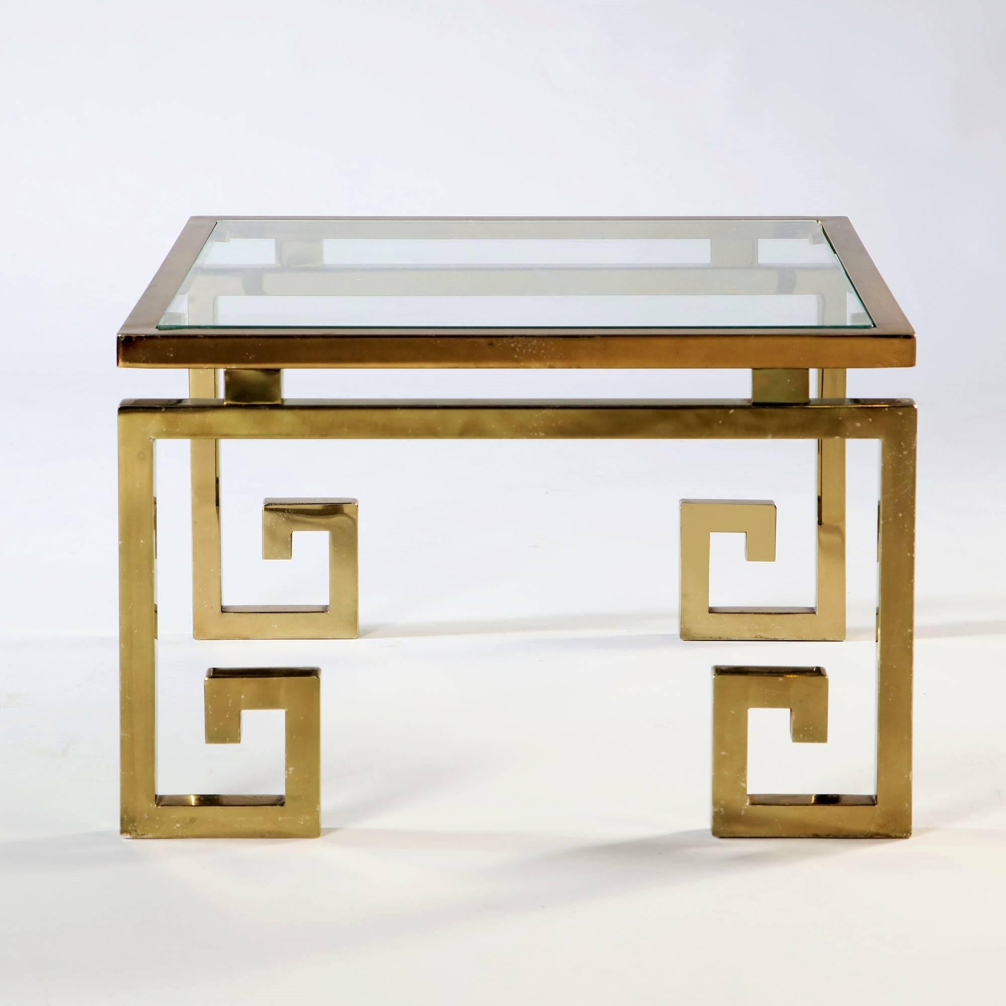 A brass occasional table in the manner of Maison Jansen with stylised Greek key feet and a glass top.