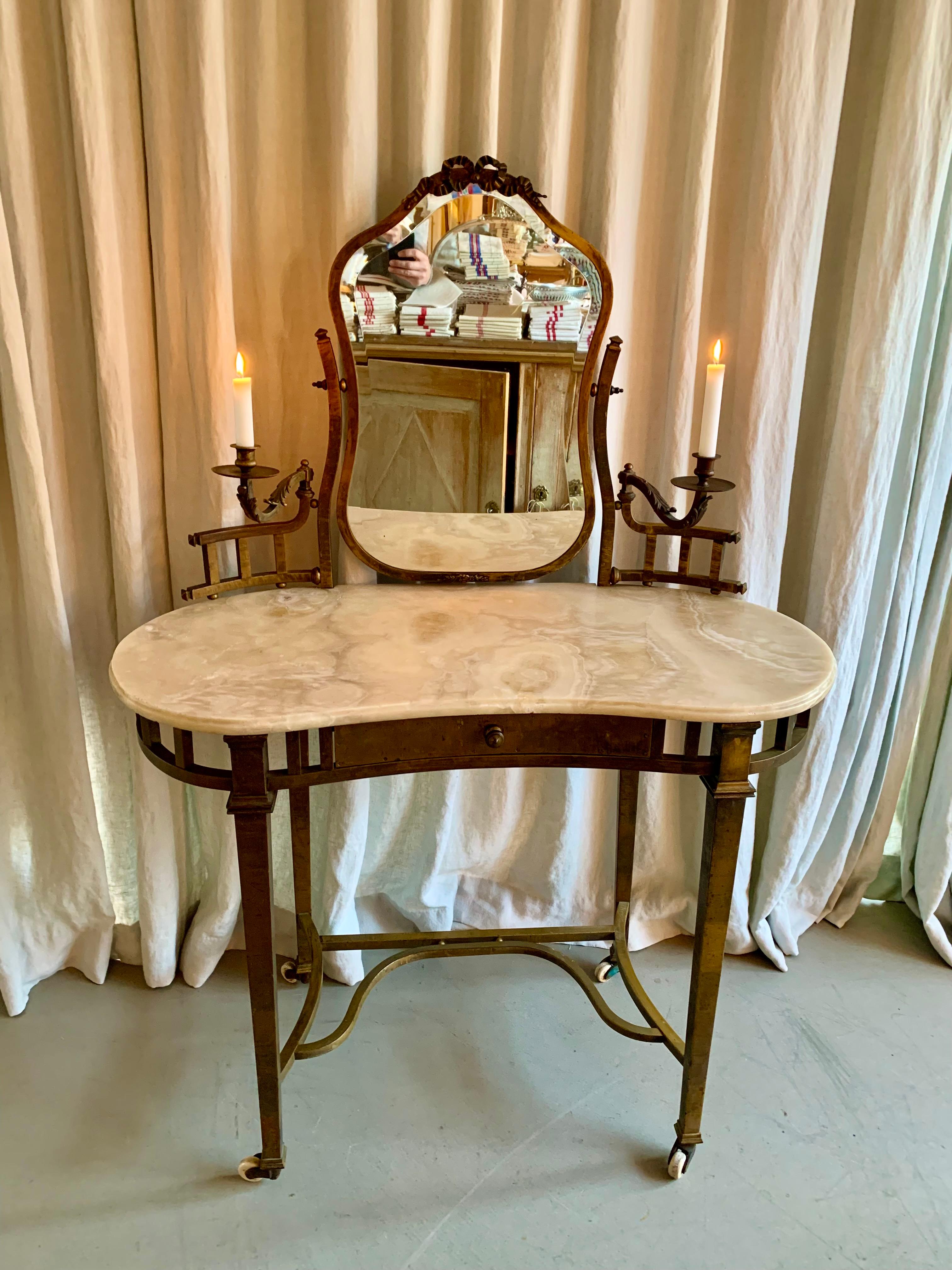 Gorgeous antique French patinated brass vanity with beautiful onyx kidney shaped table top. The elegant vanity has 2 light holders for candles and a drawer plus many fine ornamented details.
