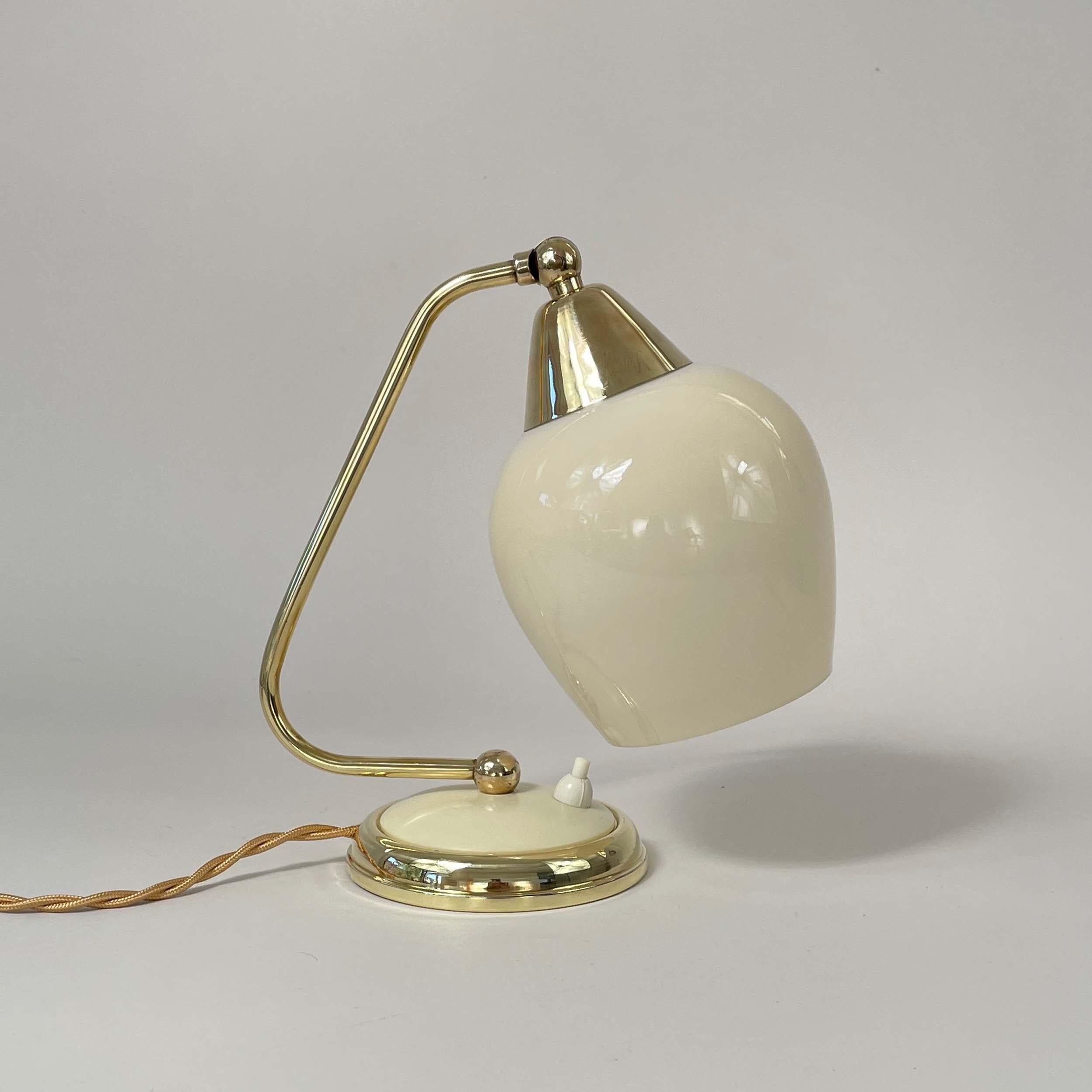 Cette lampe de table vintage du milieu du siècle a été conçue et fabriquée en Allemagne dans les années 1950.

Le luminaire présente un design épuré avec un cadre en laiton poli et un abat-jour réglable en opaline crème. Elle est dotée d'un