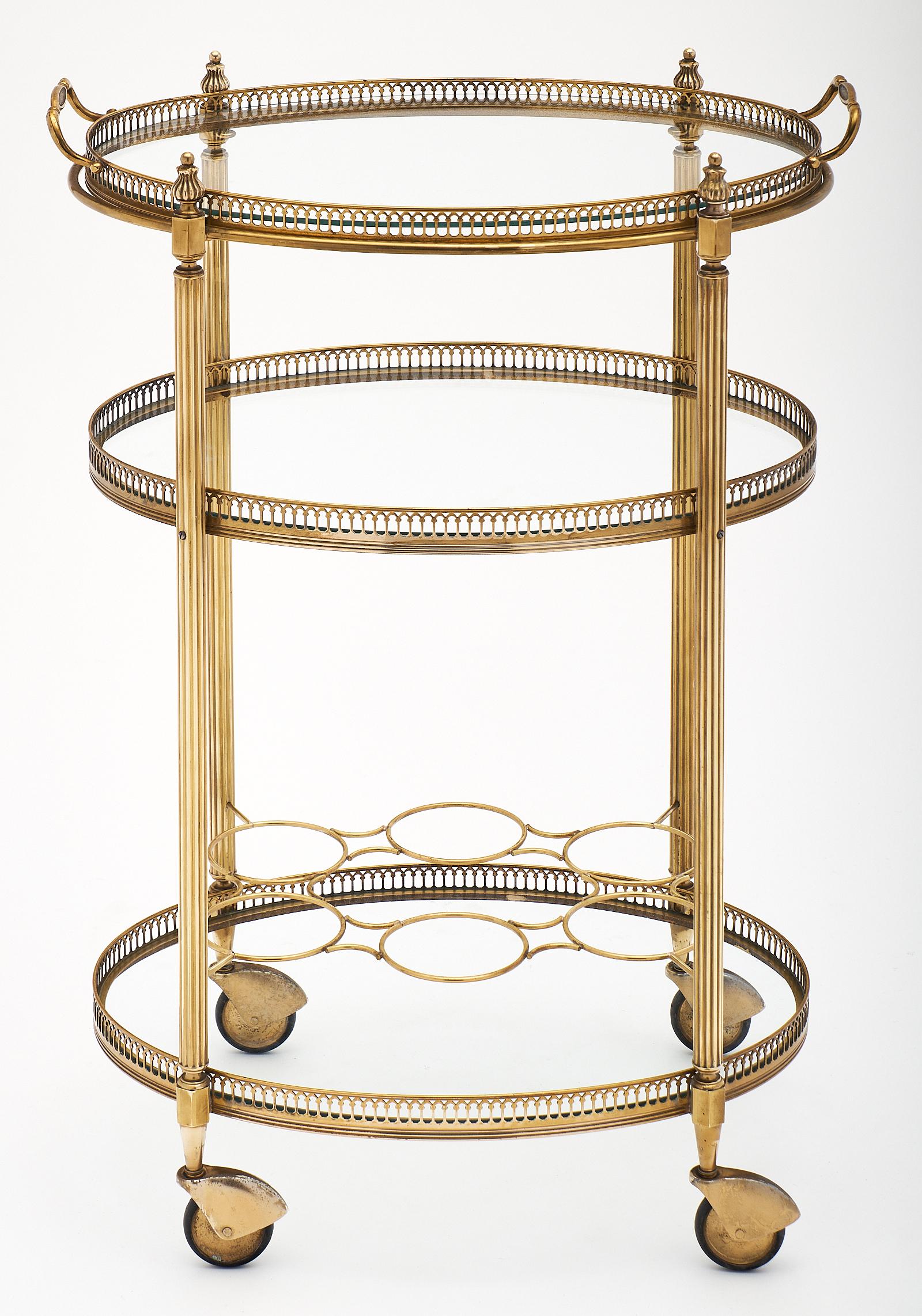 French Art Deco period brass bar cart featuring three glass shelves. Each tier has a brass gallery, and the bottom shelf has a bottle holder. The top is a detachable tray for use while entertaining! It is on the original casters, both functional and