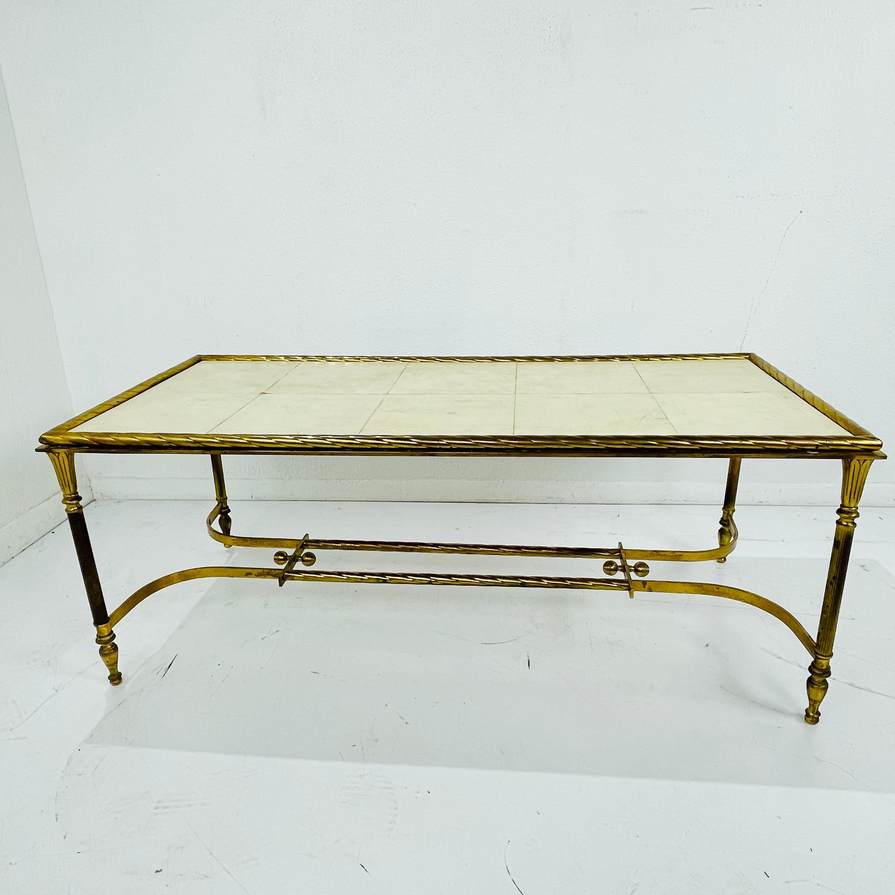 Elegant French cocktail table featuring a solid cast brass frame with a large parchment + wood tabletop. The brass is beautifully golden patinated with some oxidation spots, the parchment shows some raising at edges, scratches, and other wear due to