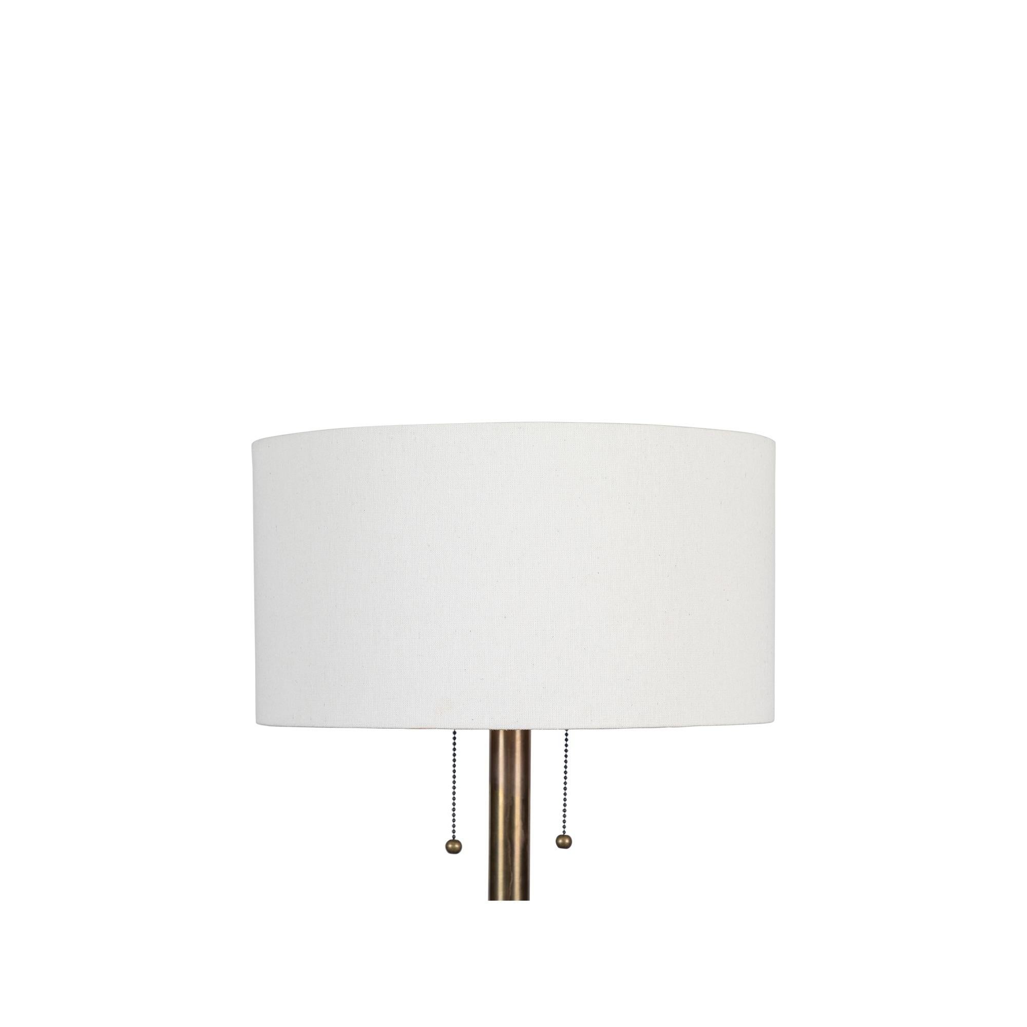 The Paul floor lamp is a solid brass floor lamp with a linen drum shade. The lamp has two separate pull chains so the bulbs can be turned on or off independently and features small, round, brass feet and finial. The cord is wrapped in brown