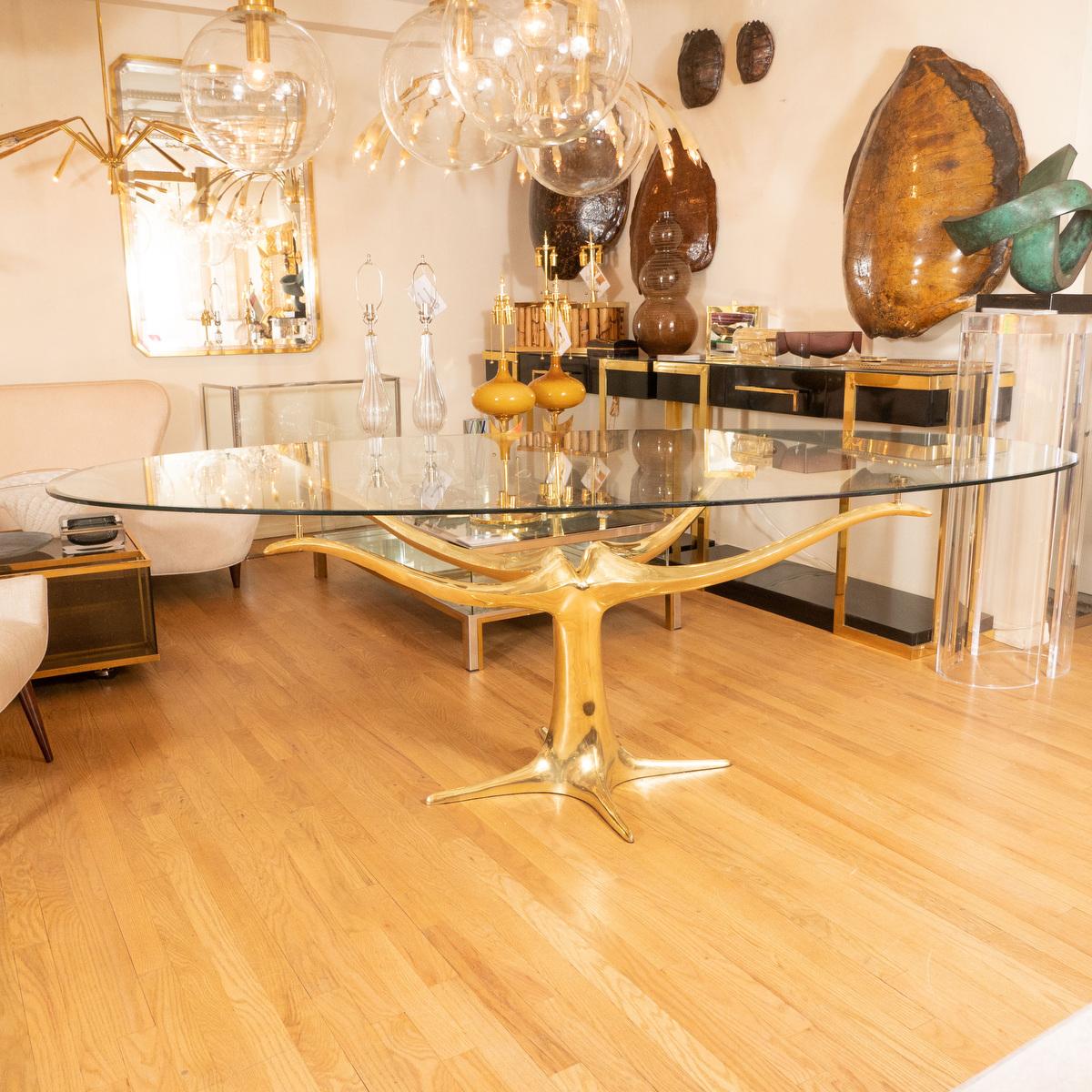 Brass pedestal base dining table with oval glass top.