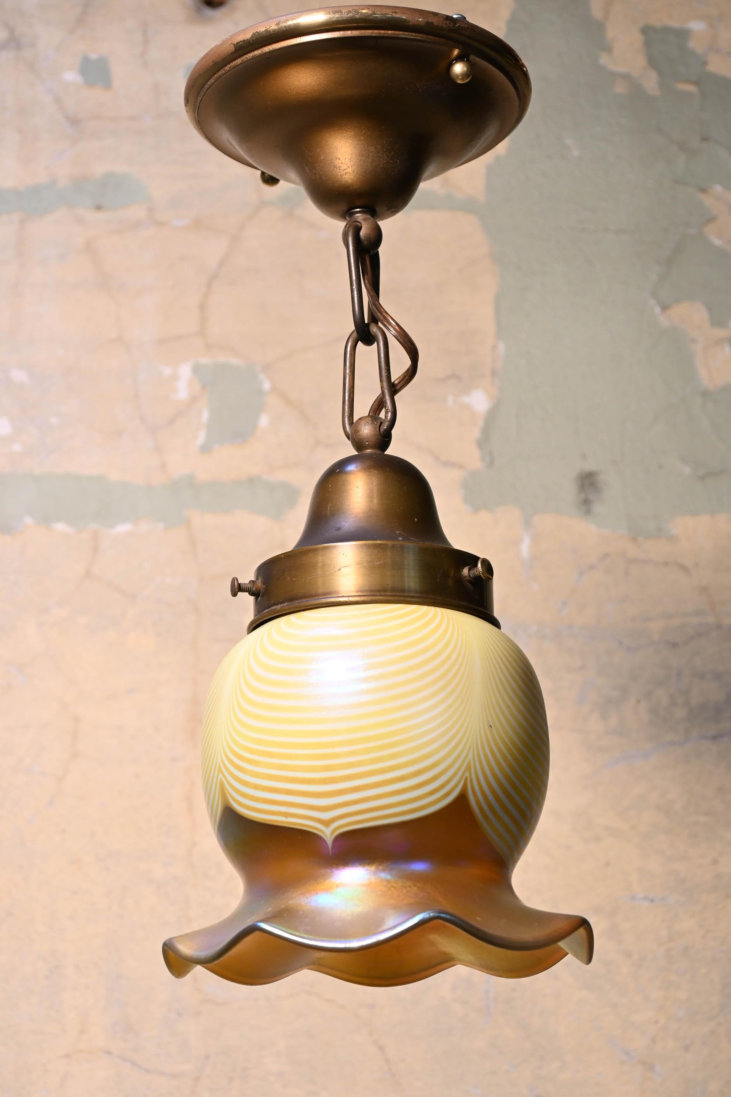 This shade is of the pulled feather variety. Cream and yellow feathered layers reach down to the multi-colored glass of the skirted rim. This fixture is larger than most with 3” fitter size. Paired with a simple brass fixture, the shade is the