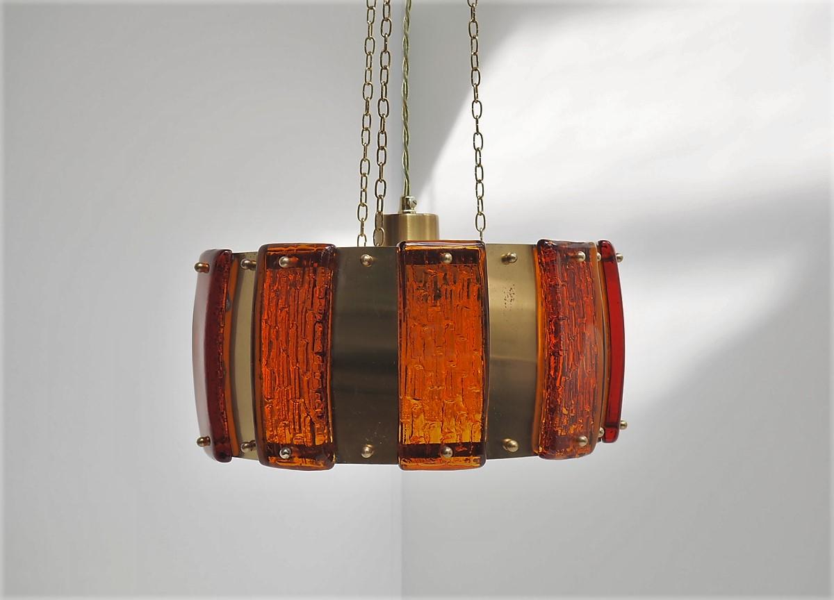 Brass pendant decorated with thick amber colored glass pieces, midcentury design from the Danish company Vitrika.

The glass pieces have a really nice pattern that makes the light shine amazing from this pendant. In the center it has a glass shade