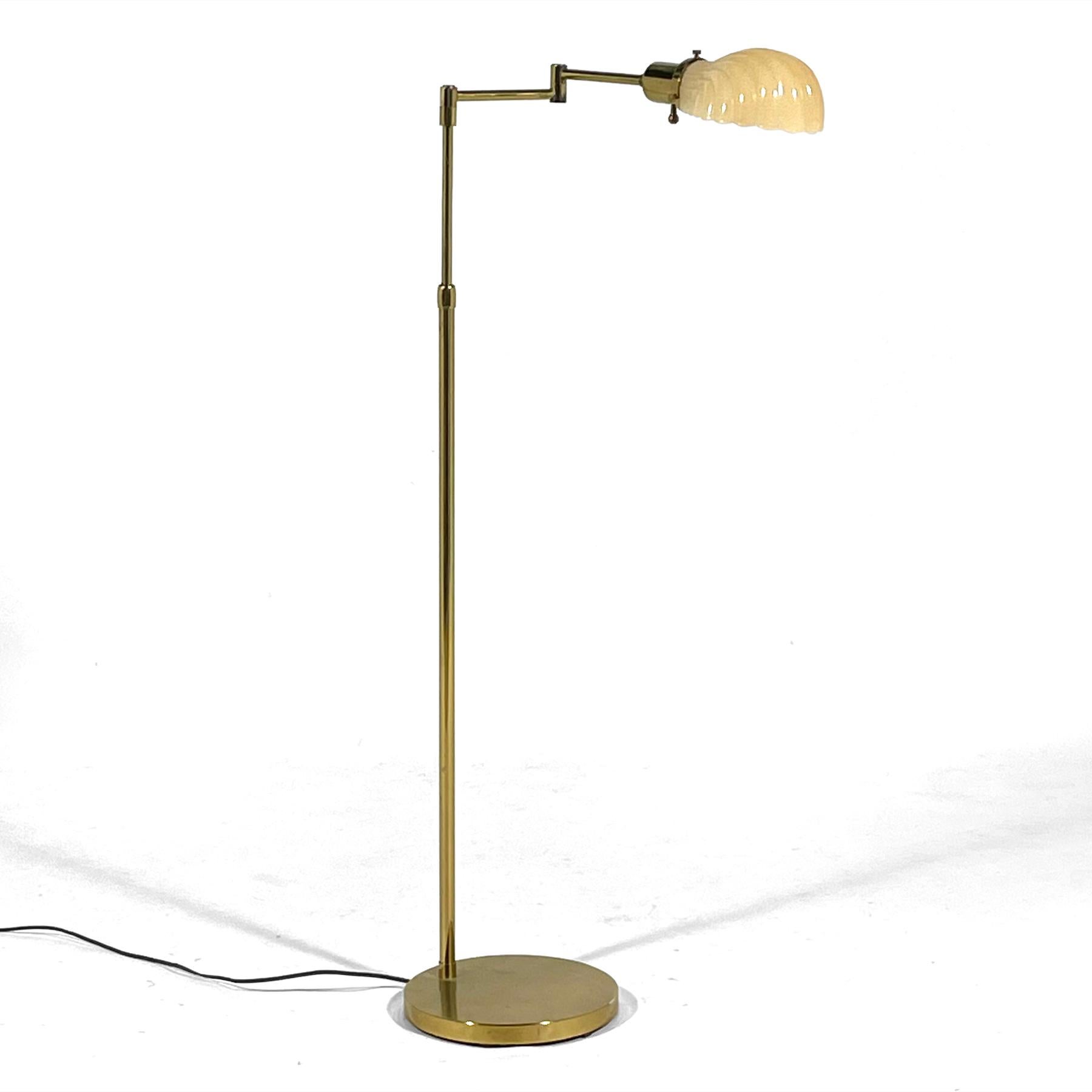 This pharmacy floor lamp is adjustable in height, has an articulating arm and features an elegant shell-shaped glass shade in a Venetian grotto style. The long column shaft is mounted to round weighted bases and the brass has a beautiful aged