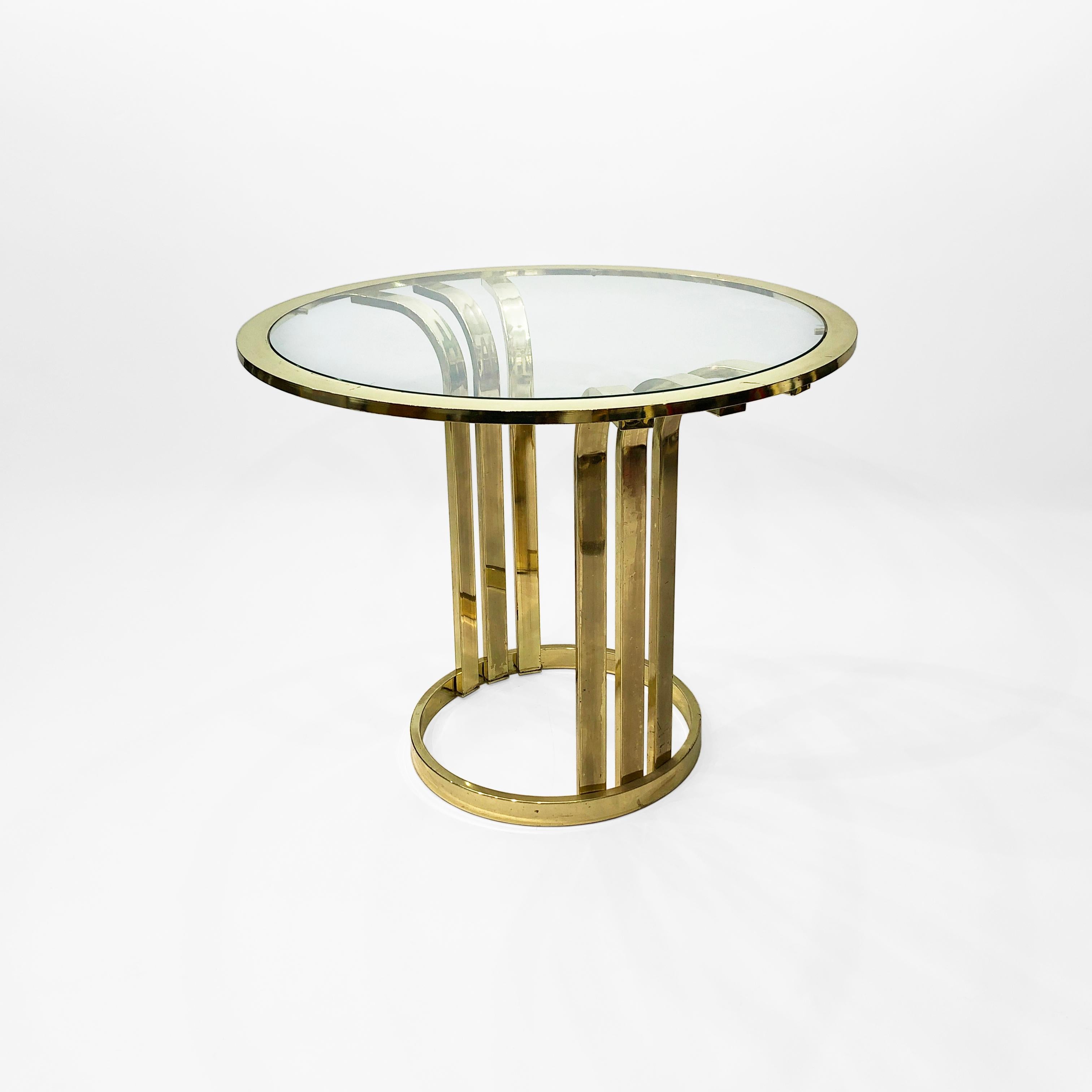 An elegant Art Deco-inspired side or entryway table, consisting of an organic, curved goblet shaped brass-plated frame, supporting a pane of circular glass at the top. The three-winged form of the base is very reminiscent of the 1930s – but this