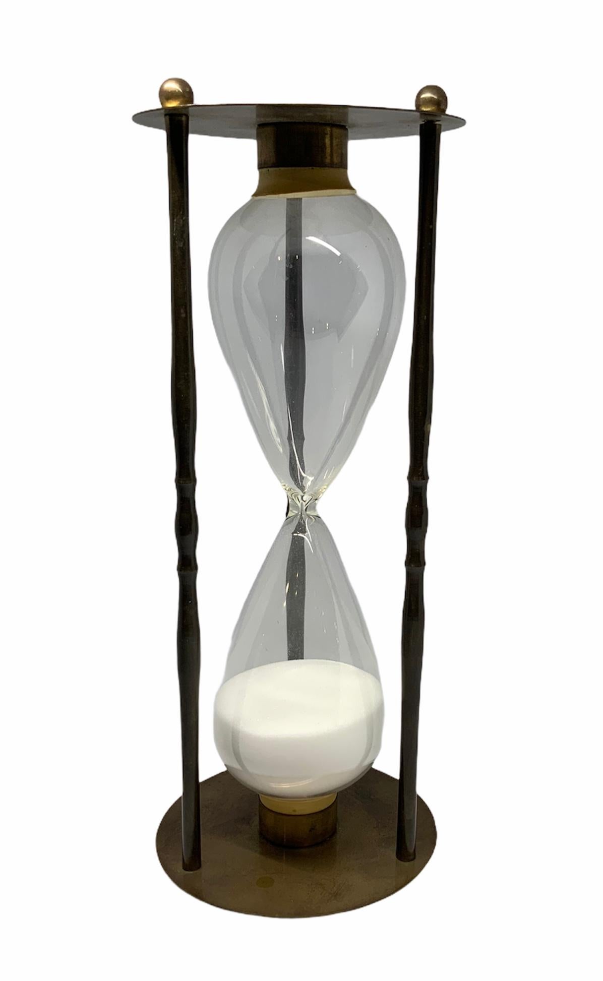 This a sand clock made with glass and brass. Two round brass plates joined by three brass columns semi-enclosed the eight shaped glass containing the sand. Three small brass sphere serve as feet. The timer lasts 30 minutes.