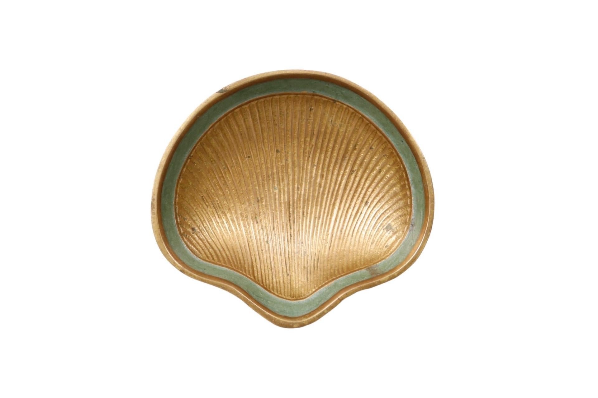 A scallop shell shaped soap dish made of brass. Trimmed with a verdigris band around the inner lip and raised on ball feet.

