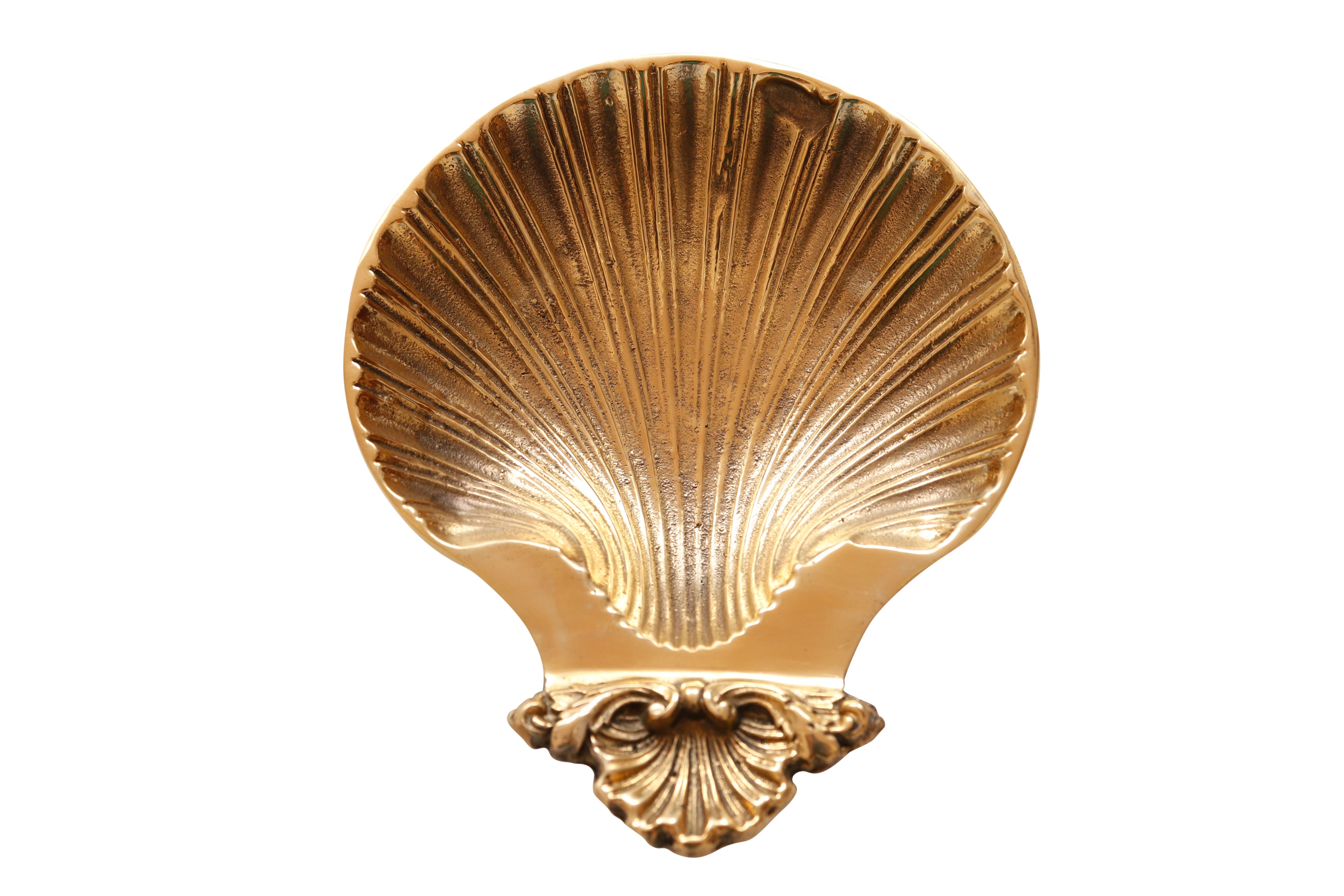 A rocaille style pressed brass soap dish, shaped like a scallop shell. Stands on three brass feet with rubber covers.
 