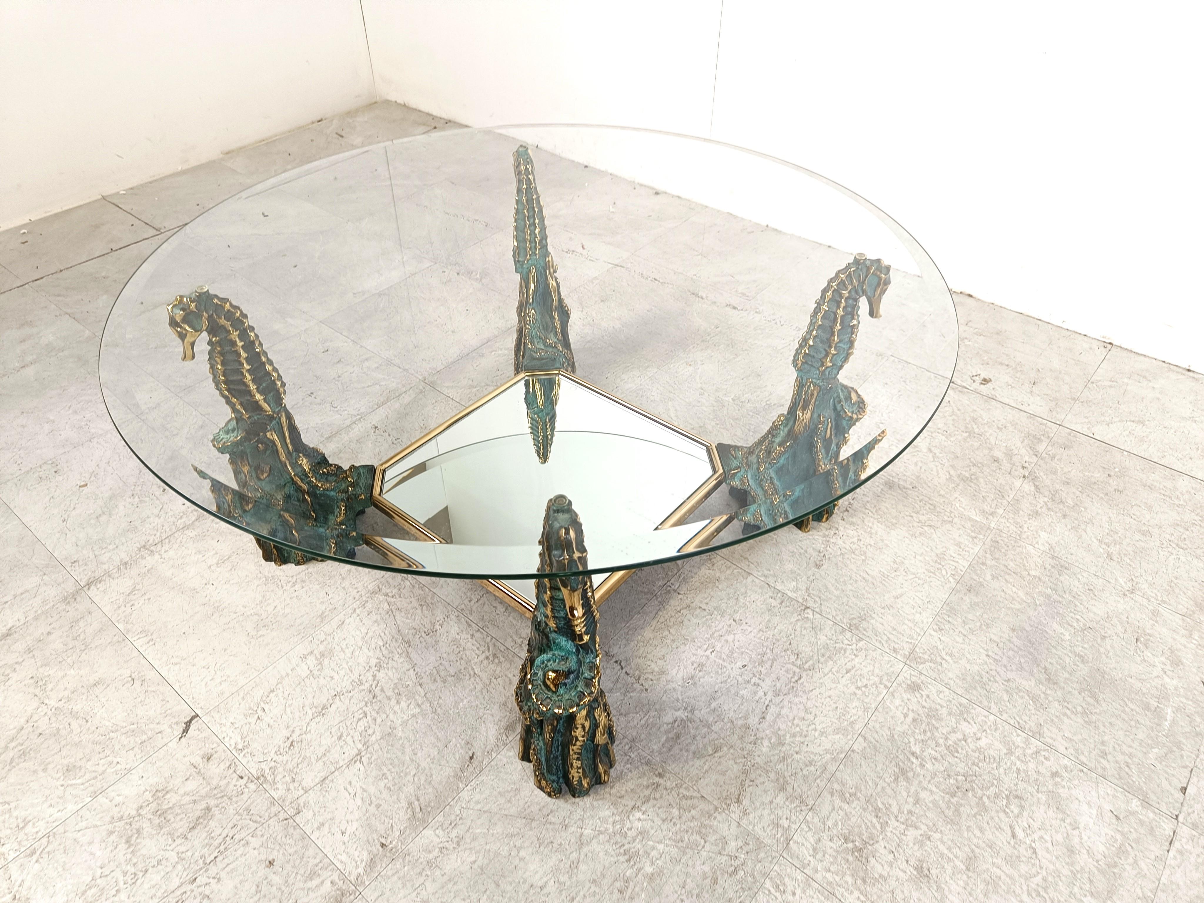 Sculptural brass bronzed seahorse figure coffee table with a round clear glass top and a mirrored glass lower shelf.

In the style of Maison Jansen

Made in Belgium in the 1960s 

Good condition

Height: 42cm/16.53