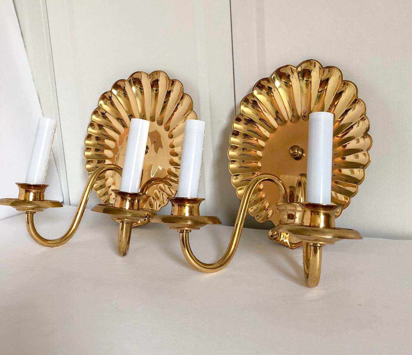Handsome pair of vintage solid brass shell-motif escutcheon wall sconces with double arms. The candle sleeves are new. Includes mounting plate for hardwiring. Original wiring in working condition; a 40 W chandelier bulb is recommended for each arm.