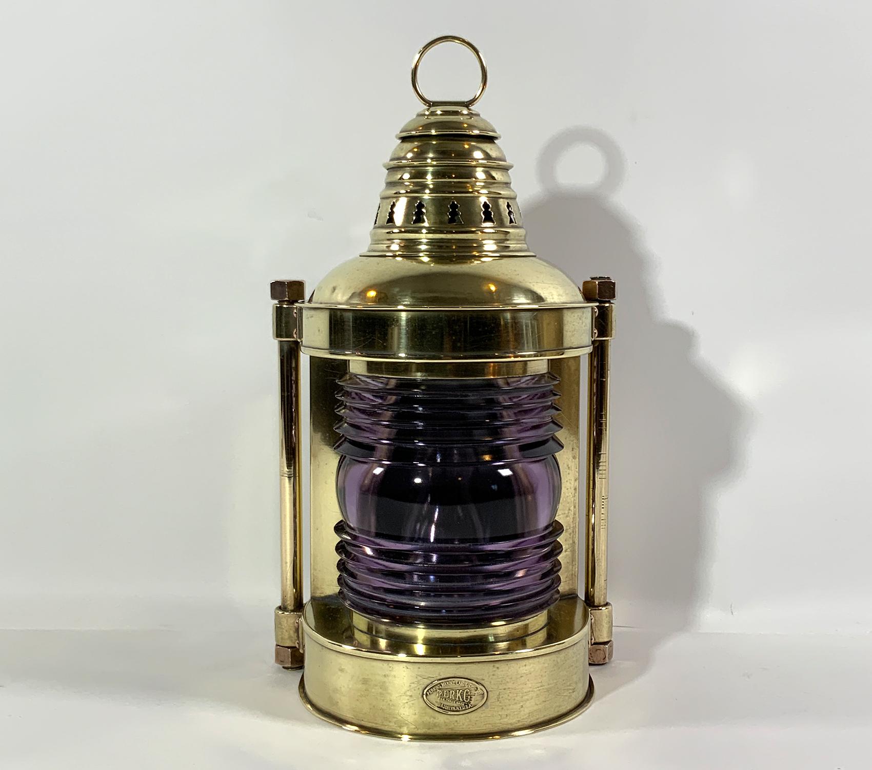 Heavy brass masthead lantern with makers badge tag from Perkins Marine of Brooklyn, New York, Perko. The Fresnel glass lens has turned to a shade of light lavender. Heavy brass bars are fitted to the side mount rings. Vented top with carry ring.