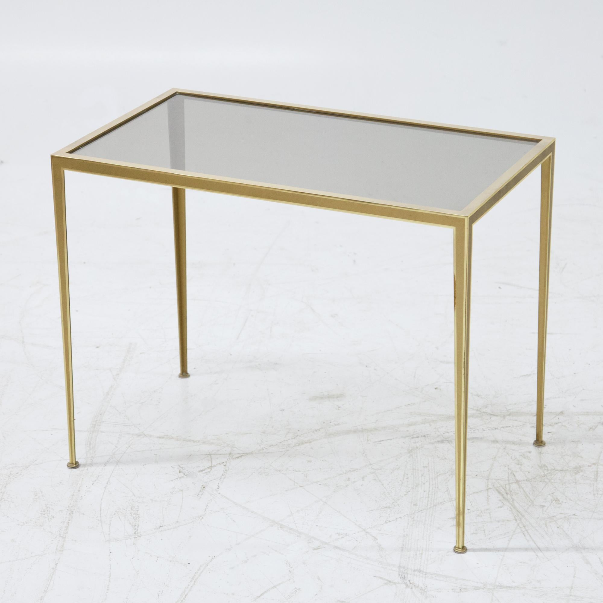 Decorative side table made of brass with smooth, pointed legs and glass top.