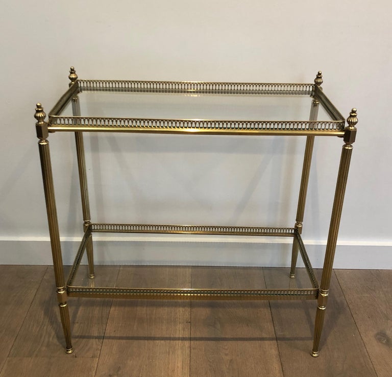 This neoclassical style side table is made of brass with two glass shelves. This end table has fluted legs, a very nice gallery surounded the top glass shelf and has four delicate finials on the corners. This is a work by famous French designer