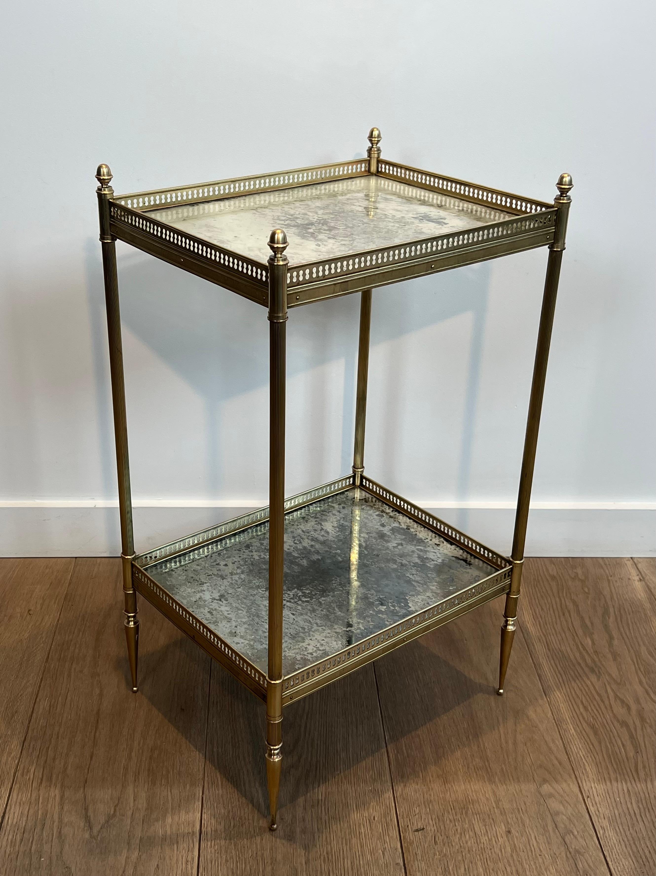 Cette très belle et élégante table d'appoint de style néoclassique est en laiton avec des plateaux en miroir oxydé. Les fins pieds coniques surmontés de tubes cannelés, reliés par deux galeries ajourées en laiton entourant de beaux miroirs églomisés