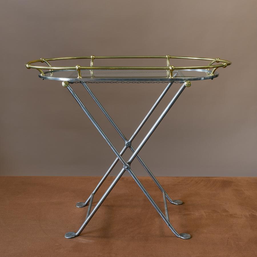 Unusual metal and glass serving tray table in waxed steel with polished brass details. Comprising of X-frame folding legs on to which the tray sits atop. The brass rail on the tray is reminiscent of the handrail on the deck of a classic