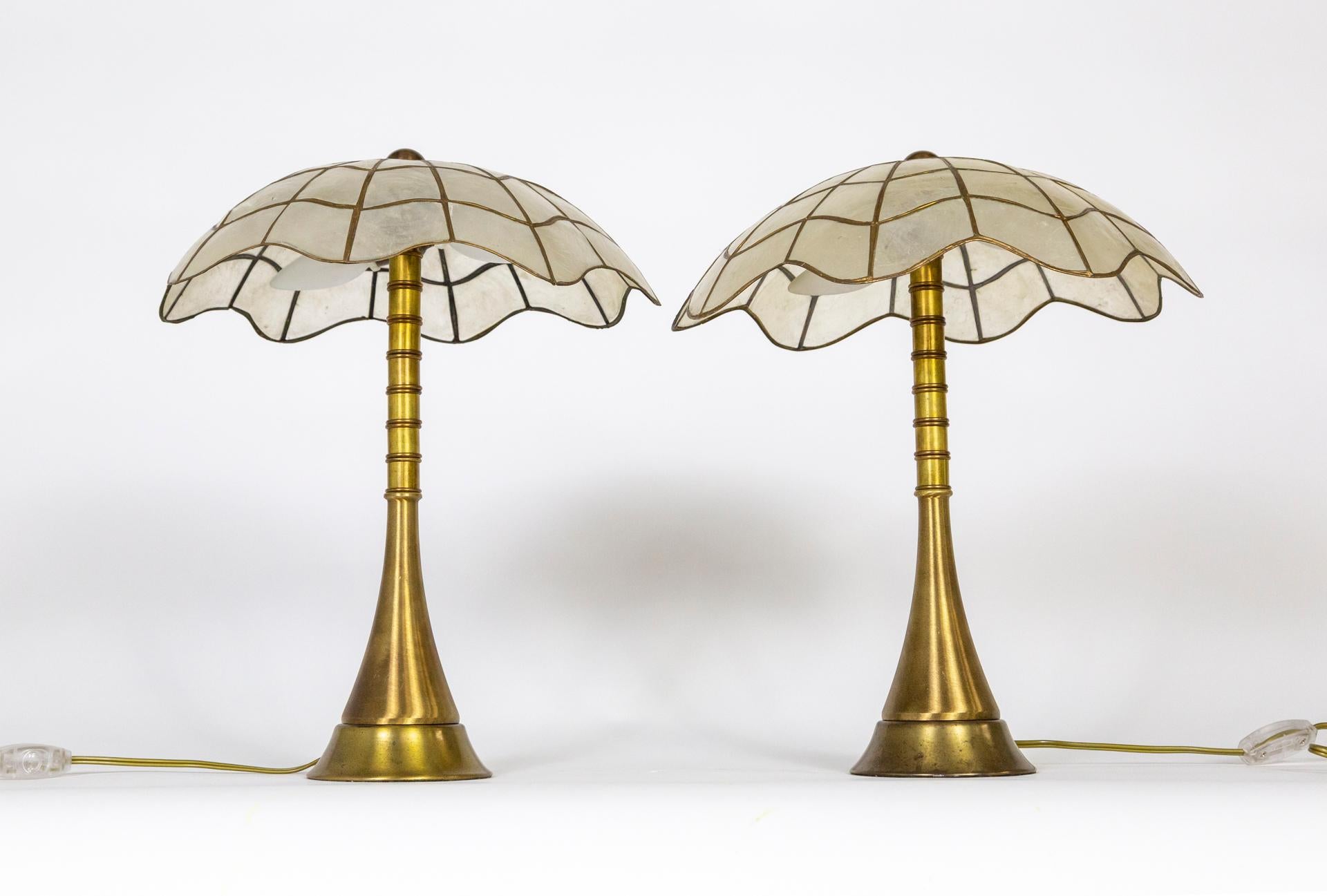A splendid pair of newly made table lamps with Hollywood Regency vibes.  They have sleek, trumpeted stems with banded details and mosaic capiz shell shades in a scalloped, umbrella shape. The illumination through the shell is lovely. They each have