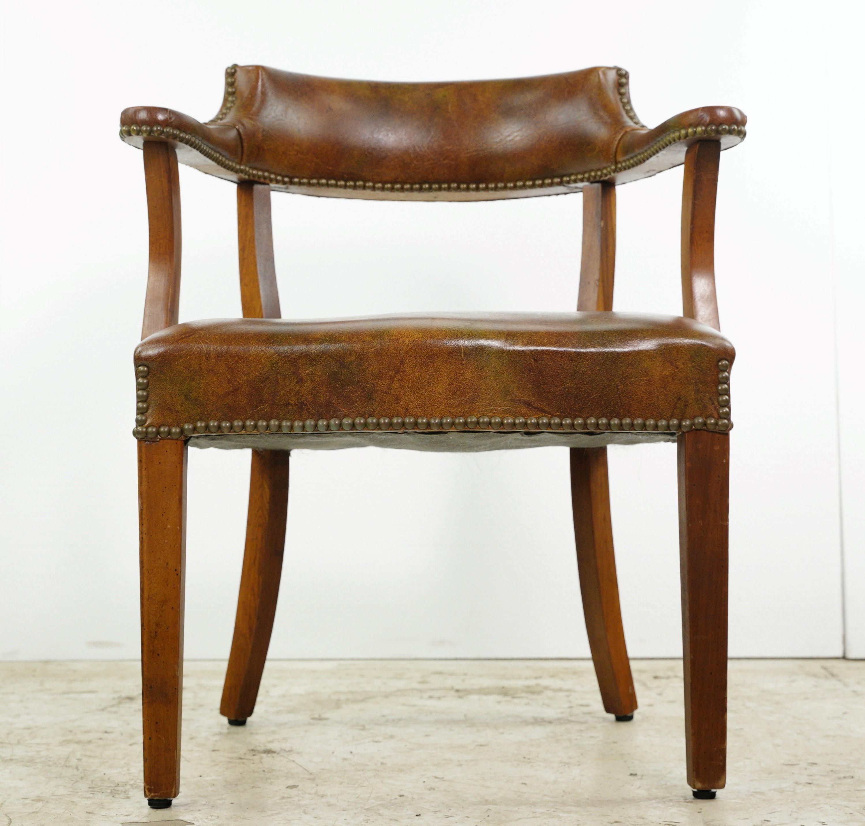This Mid-Century Modern style studded brown vinyl covered wood frame office arm chair is a classic piece. With its brass studs and brown upholstery, it exudes timeless elegance. The wood frame adds a touch of warmth, making it a stylish and
