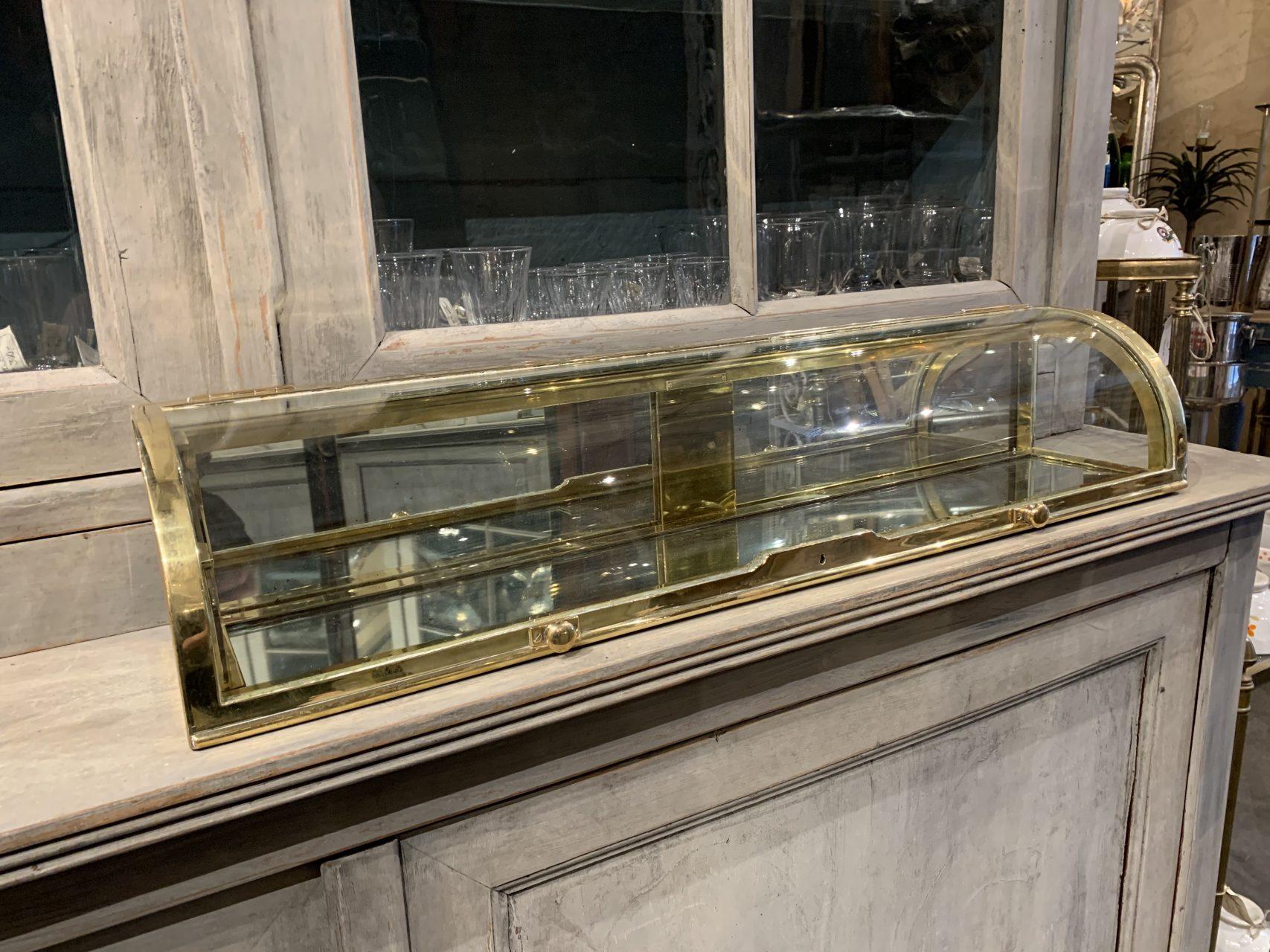 Coveted and most presentable antique French brass table montre, from circa 1880-1890. Elegantly curved glass lid and mirrored glass cladding. Gorgeous handsome profile. The display case was originally quality boutique inventory, and is in super