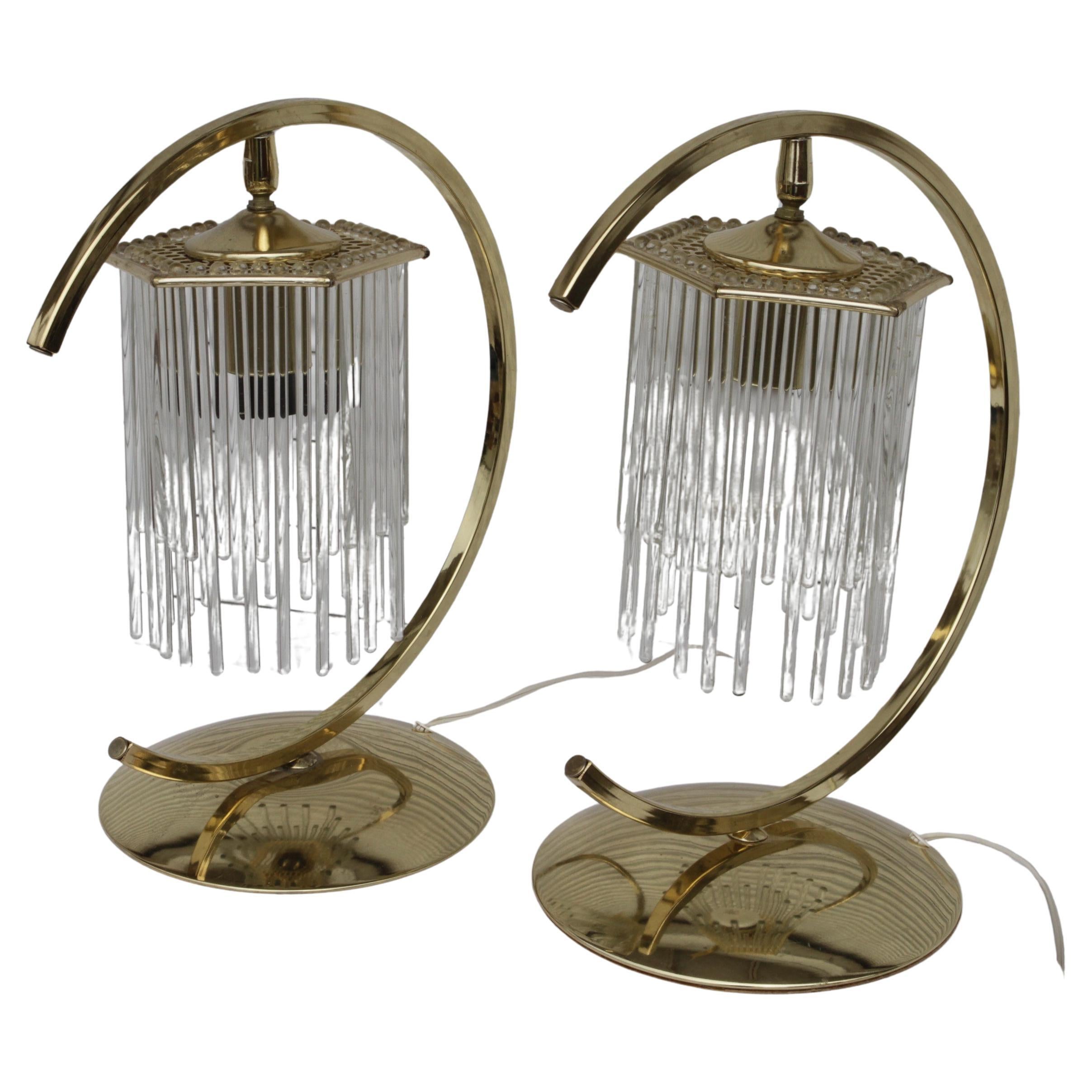 Cette lampe de table respire l'élégance avec son cadre en laiton unique en forme de croissant, qui s'incurve gracieusement autour du luminaire central. Suspendu au sommet, un étonnant ensemble de tiges de verre verticales, disposées en cascade à la