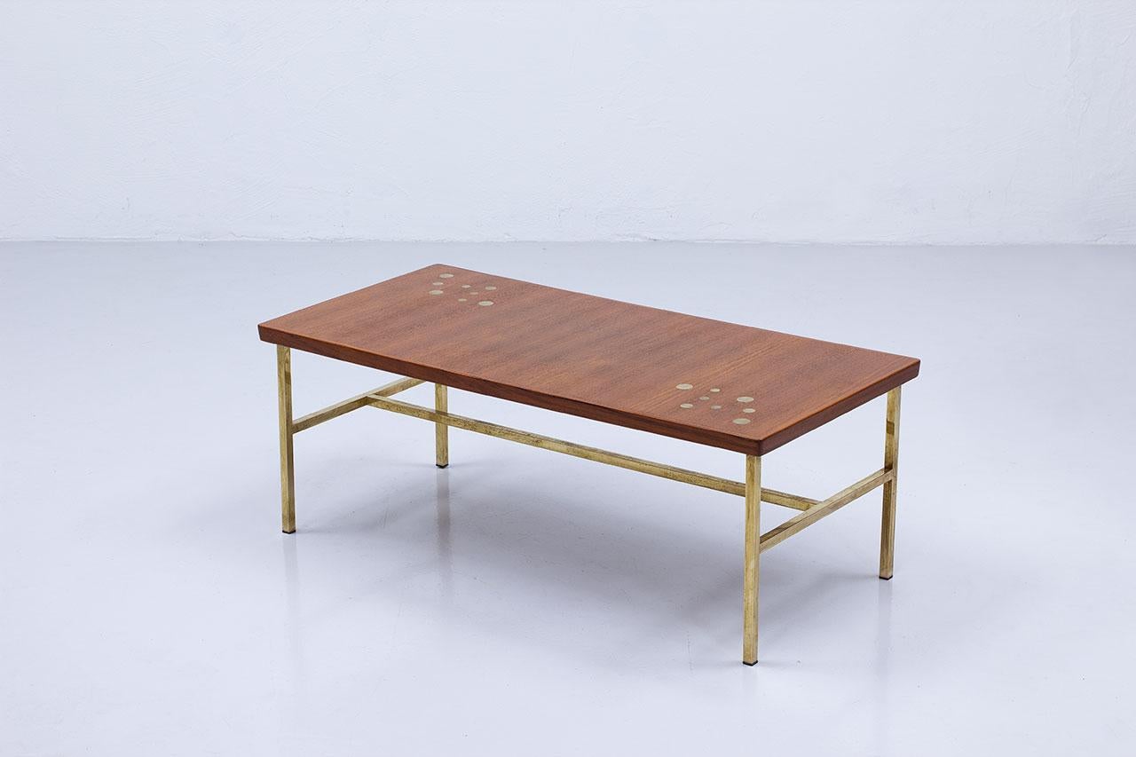 Eleganter Couchtisch/Sofatisch. Hergestellt in Schweden, höchstwahrscheinlich in den 1960er Jahren. Die Tischplatte ist aus Teakholz und hat Messingintarsien. Der Sockel besteht aus quadratischen Messingprofilen. 