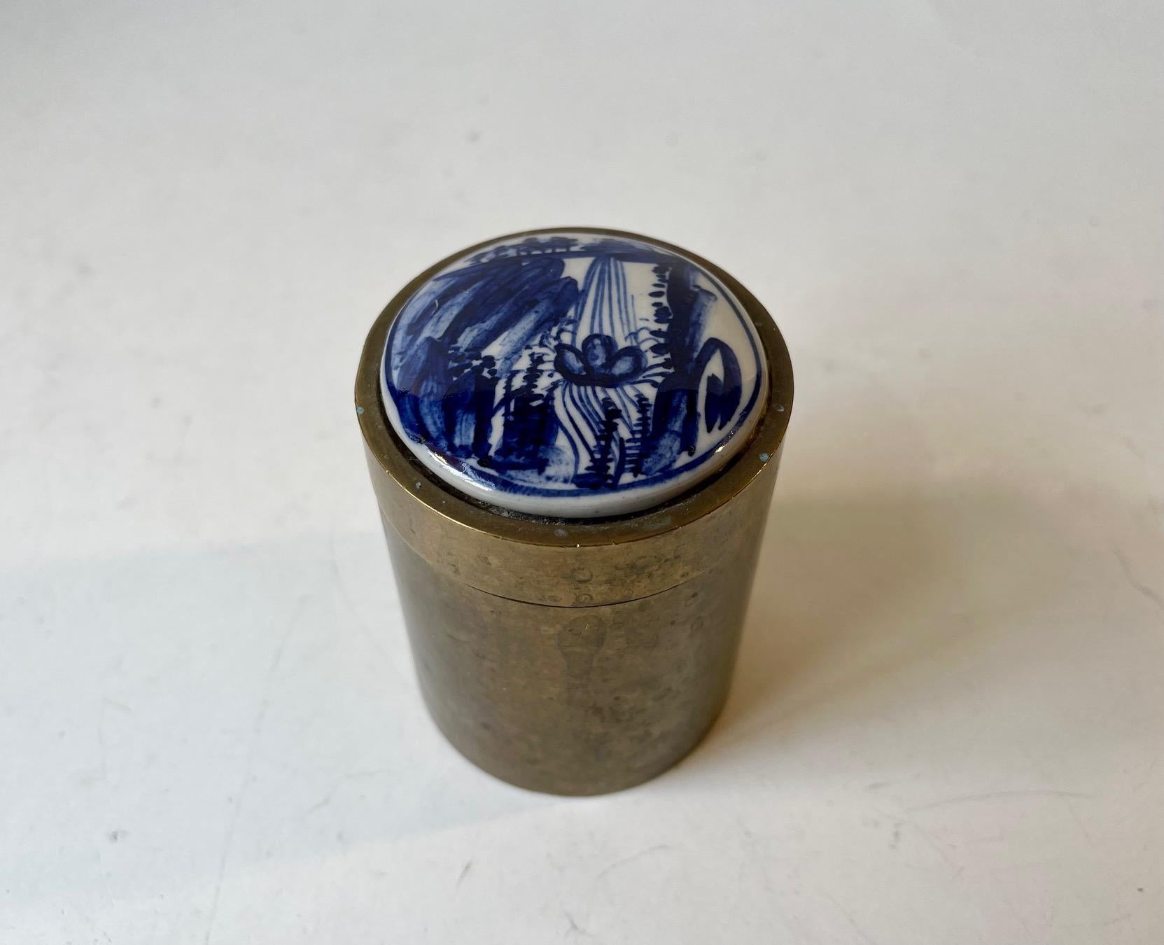 Small container for cigarettes or tobacco. Its made from Solid patinated brass and its screw-of lid is decorated with a small hand-painted porcelain platter from Delft. Measurements: H: 8 cm, D: 6 cm.