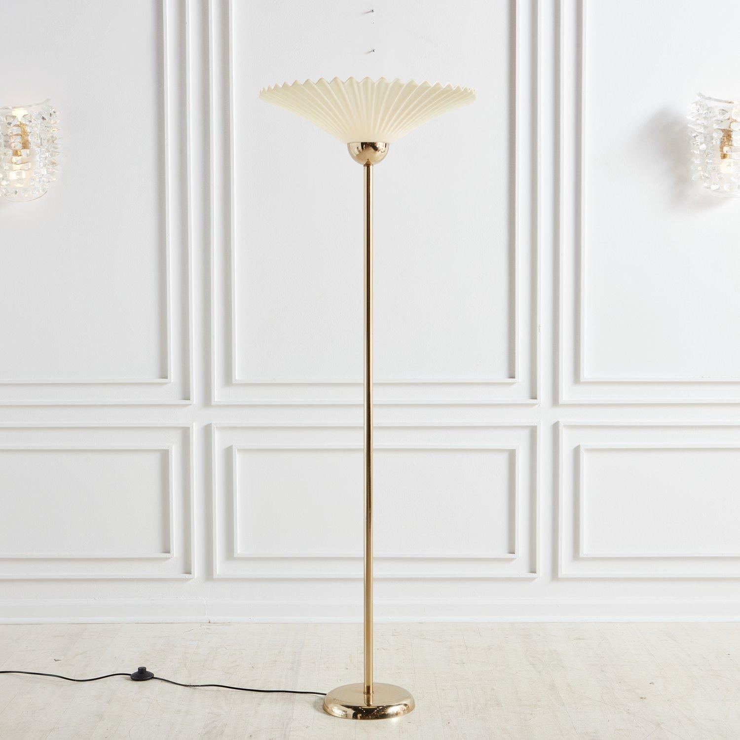 A Mid-century torchiere floor lamp featuring a large cream fanned acrylic shade. This 1960s lamp has a polished brass body with a circular brass base and retains its original foot switch.