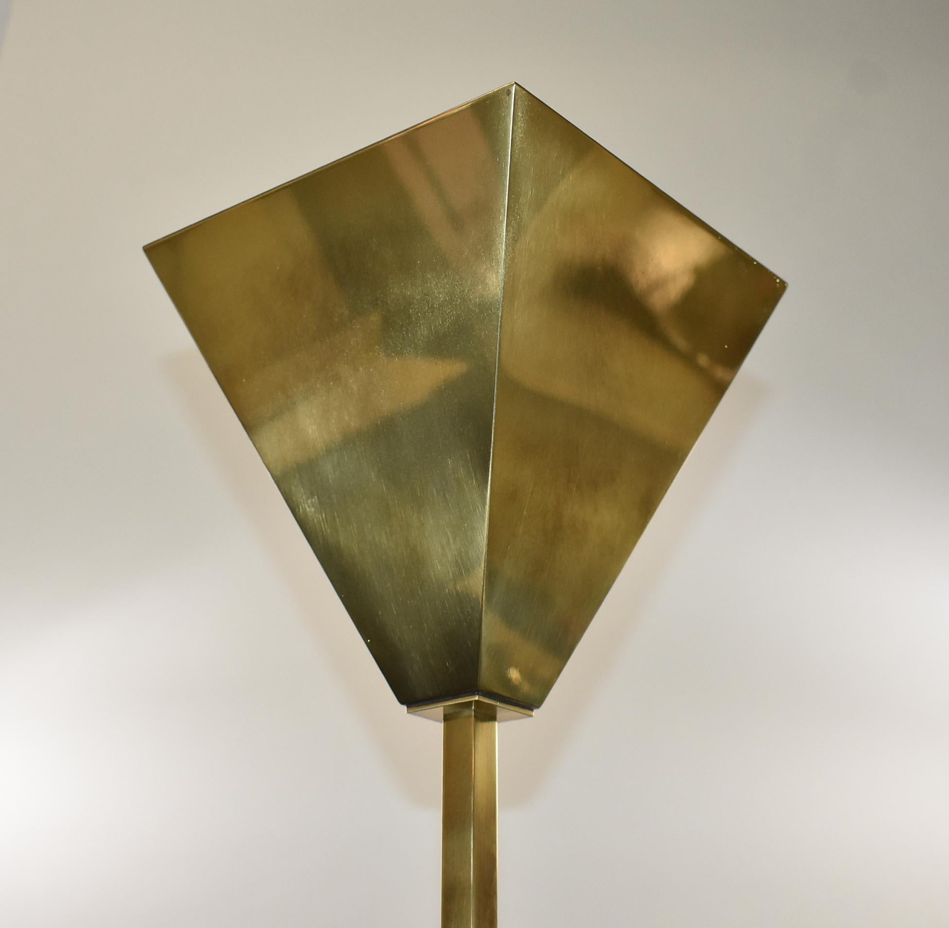 A Postmodern brass touch-on torchiere floor lamp with adjustable height, and three-way switch. This lamp is a streamlined, geometric, neoclassical design with a heavy weighted base. There is minor pitting on the base. This lamp adjusts from 51 3/4