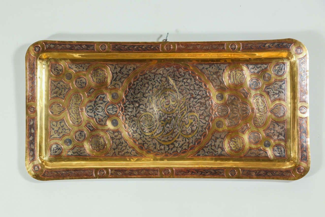 Antique Brass Tray with Arabic Koranic Calligraphy Writing.
Rectangular shape large brass tray with Islamic Koranic calligraphy writing and foliates patterns in the center.
Middle Eastern brass tray, Islamic Arabic metal artwork.
The large brass