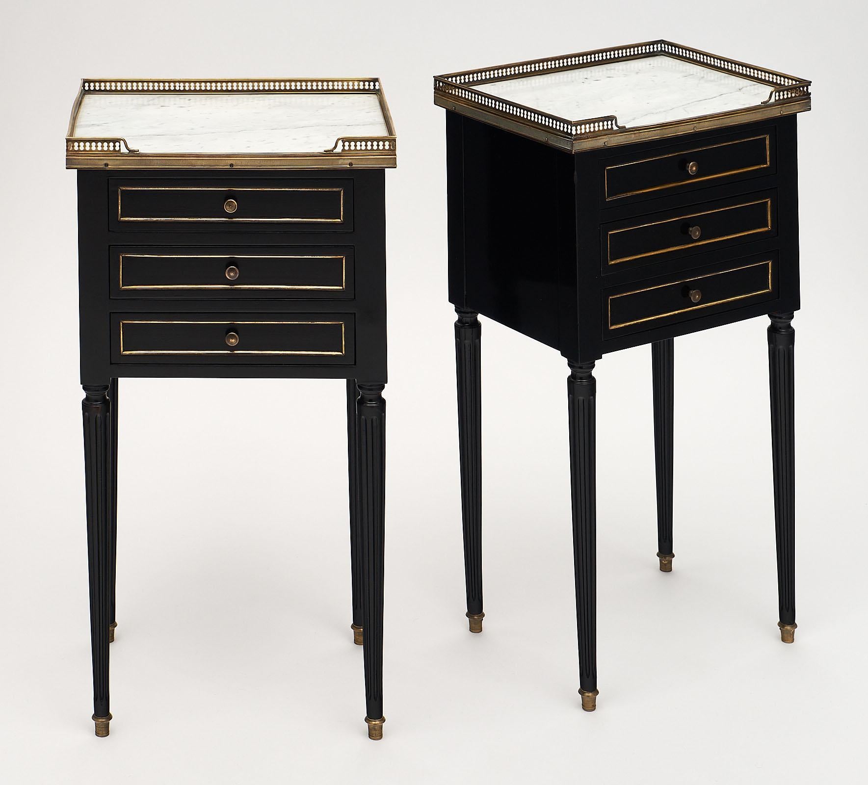 A pair of Fine Louis XVI style side tables with brass trim around original Carrara marble tops. We love the brass galleries and trim throughout, three dovetailed drawers, and original brass pulls. These tables are made of ebonized mahogany finished