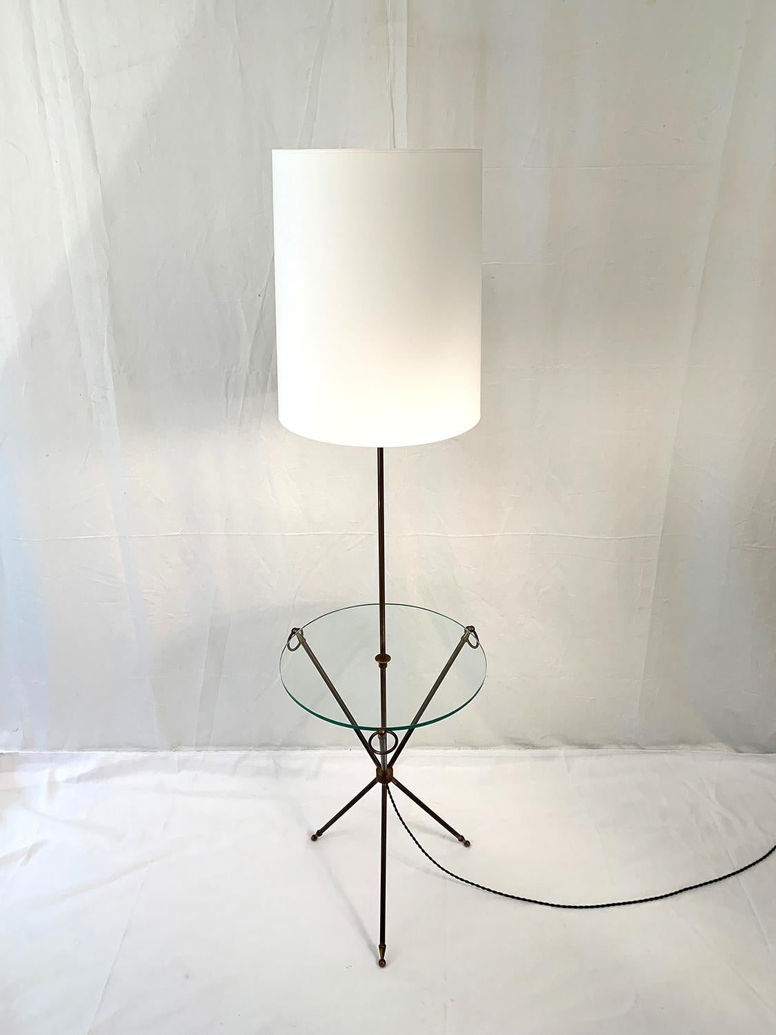 Superb brass tripod floor lamp, 1960s. The floor lamp is made of a brass tripod with loop handles, and a transparent glass on its top. The white cotton shade is new.

Superbe lampadaire trépied en laiton, 1960s. Le lampadaire se compose d'un