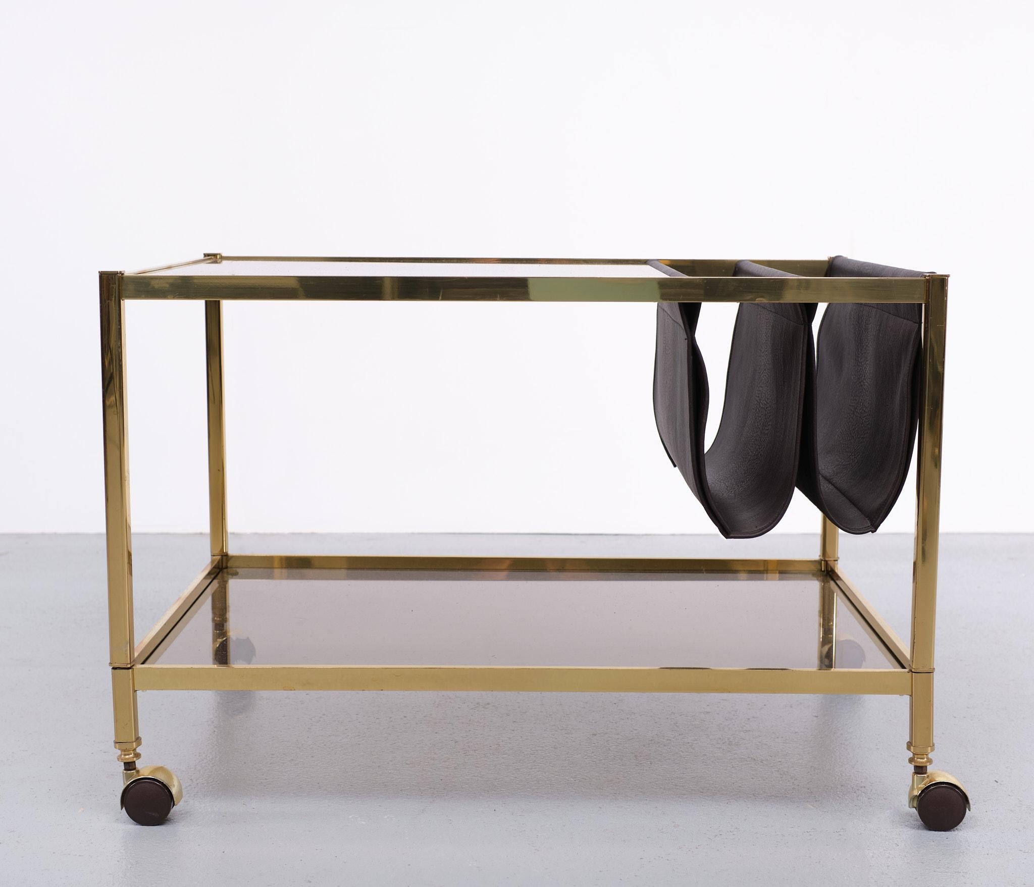 Beautiful magazine holder, trolley, side table. Three in one Love the color 
combination. Brass, dark brown leather and smoked glass tops on wheels.
Superb piece. In a good condition. Jacques Adnet in style.