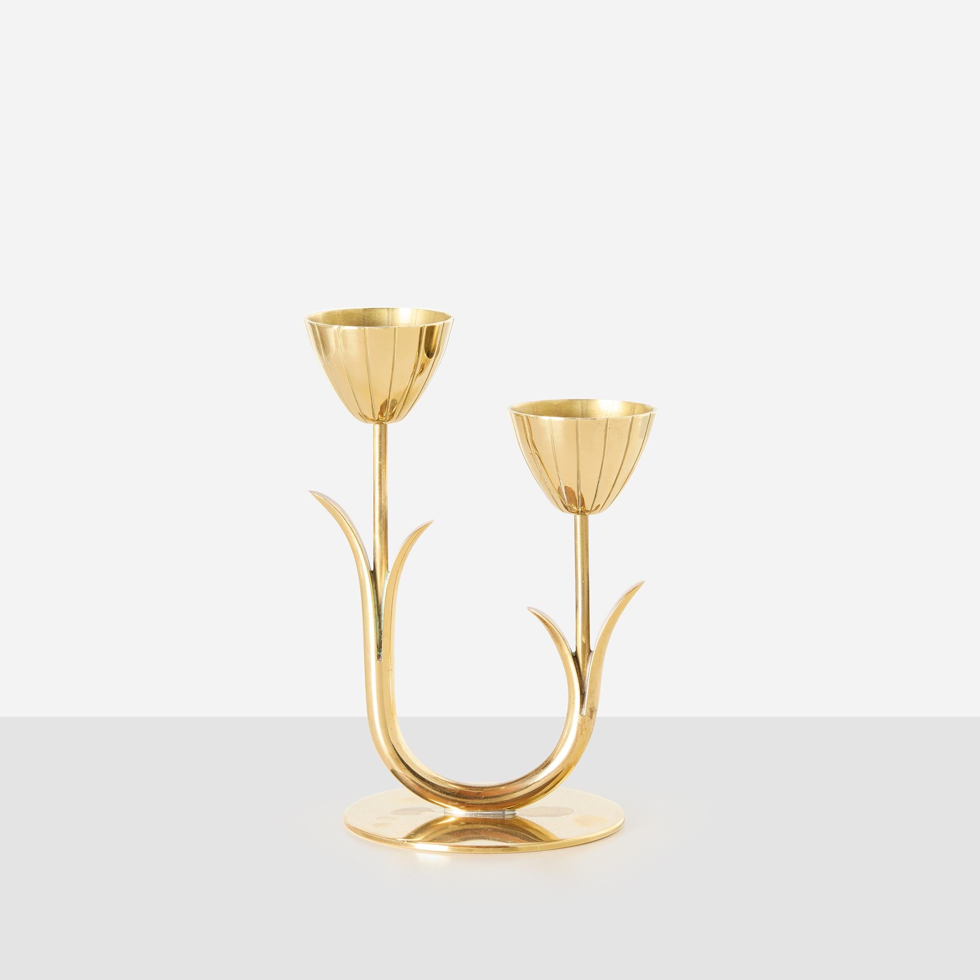 Portacandele a doppio braccio in ottone disegnato da Gunnar Ander per Ystad-Metall. Ogni coppa ha la forma di un tulipano, sostenuto da bracci a stelo con dettagli a forma di foglia. Progettato per candele di piccole dimensioni. Sul lato inferiore è