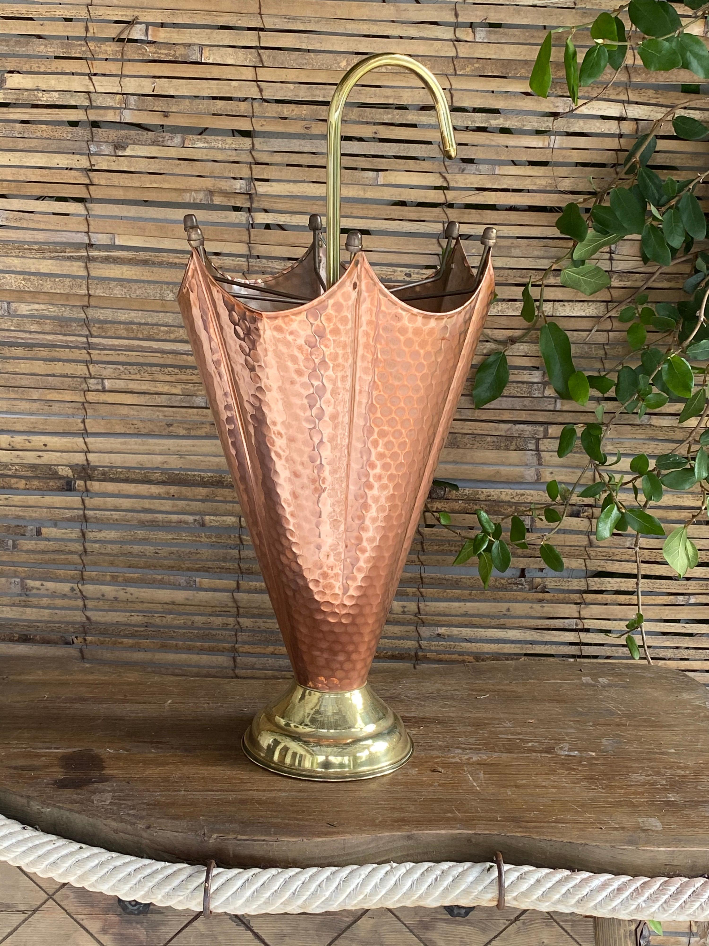 This umbrella stand is in brass and cooper. It has been made in Italy in the 1960s.
The rod and the base are in brass, and the casing is in copper.
The rod is finished at the top by a brass handle, and the shape of the object is an umbrella.
 