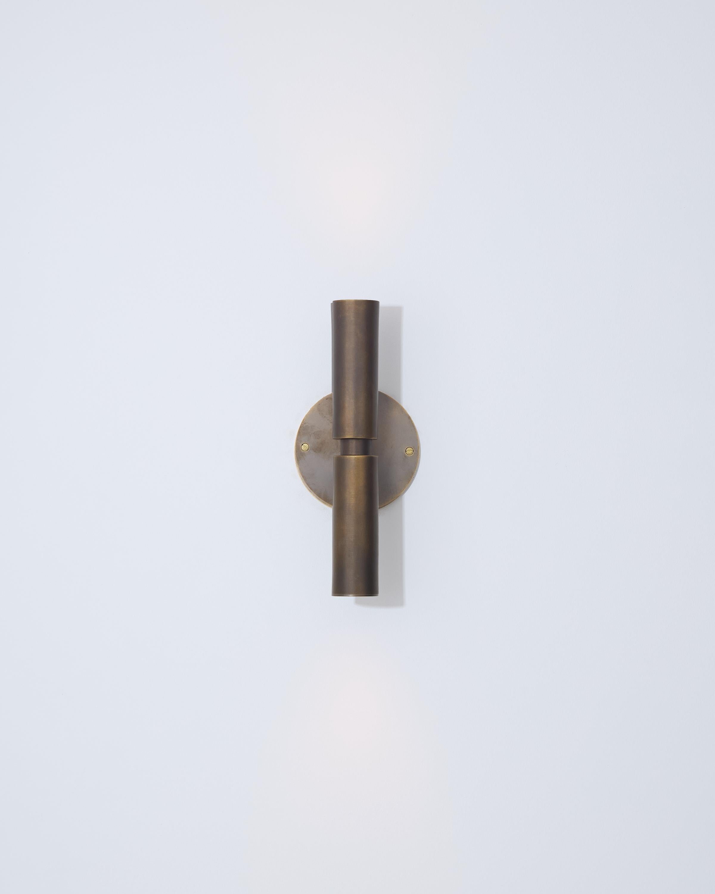 Cette applique murale présente un design à double cylindre qui fournit un éclairage vers le haut et vers le bas. Machiné en laiton massif et fini à la main dans l'une des 8 finitions design, il offre un aspect vintage, une durabilité et un profil