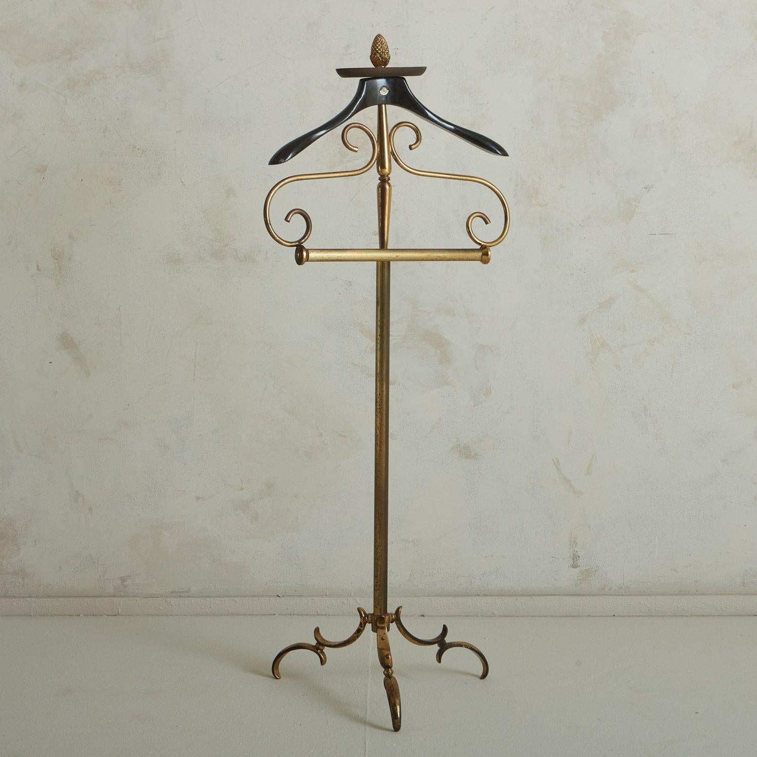 An Italian valet designed by Ico Parisi for Fratelli in the 1950s. This valet features a gilded brass frame with curled details and a tripod base. It has a black lacquered wood hanger and a catchall with a pinecone finial on the top. Retains ‘FR’