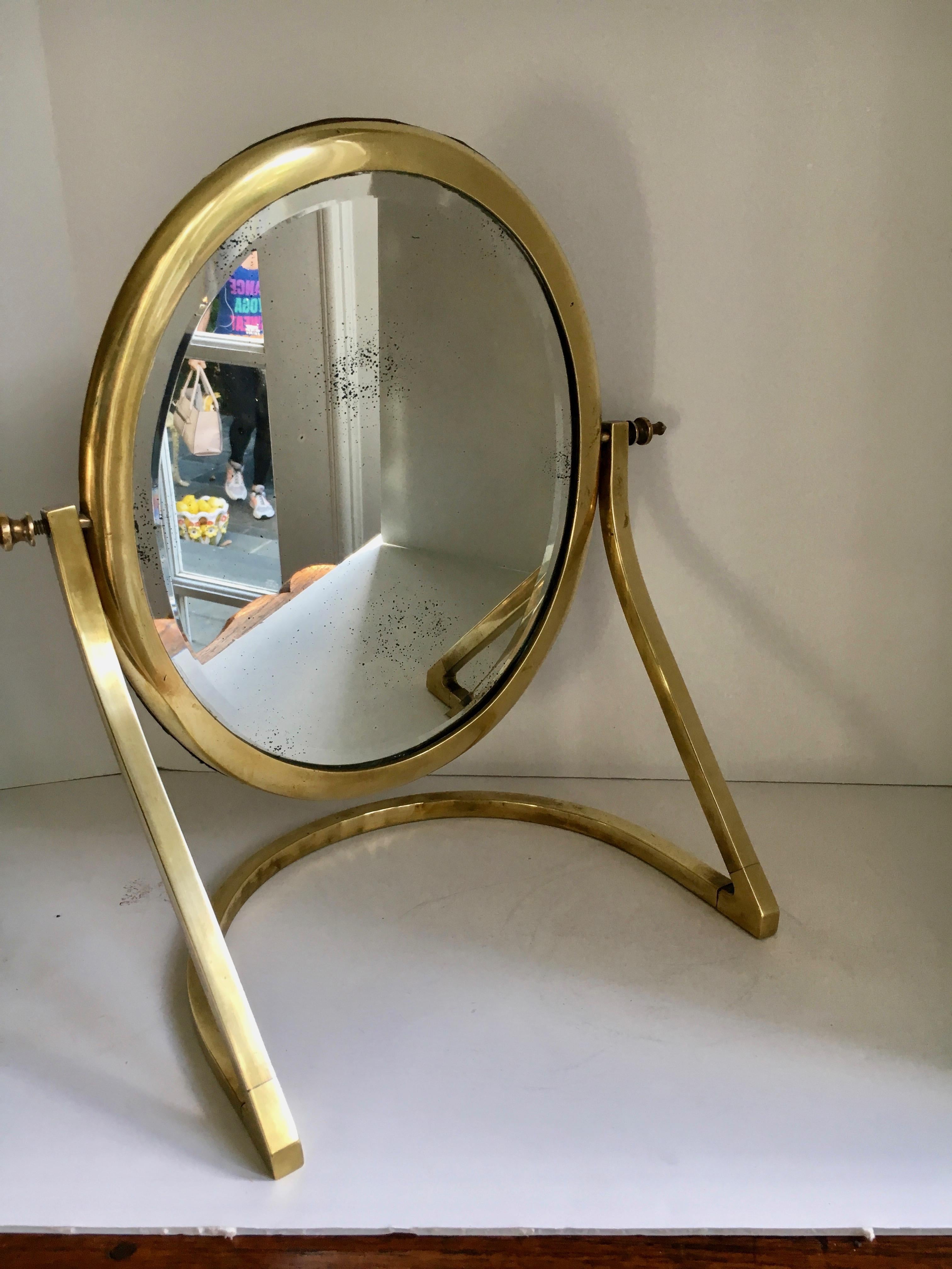 A beautiful mirror on unique stand - lovely for a ladies dressing table or handsome as for a man's closet or dressing area. The mirror is beautifully patinated. The brass finials on either side of mirror are wonderful and the rear screw closures are