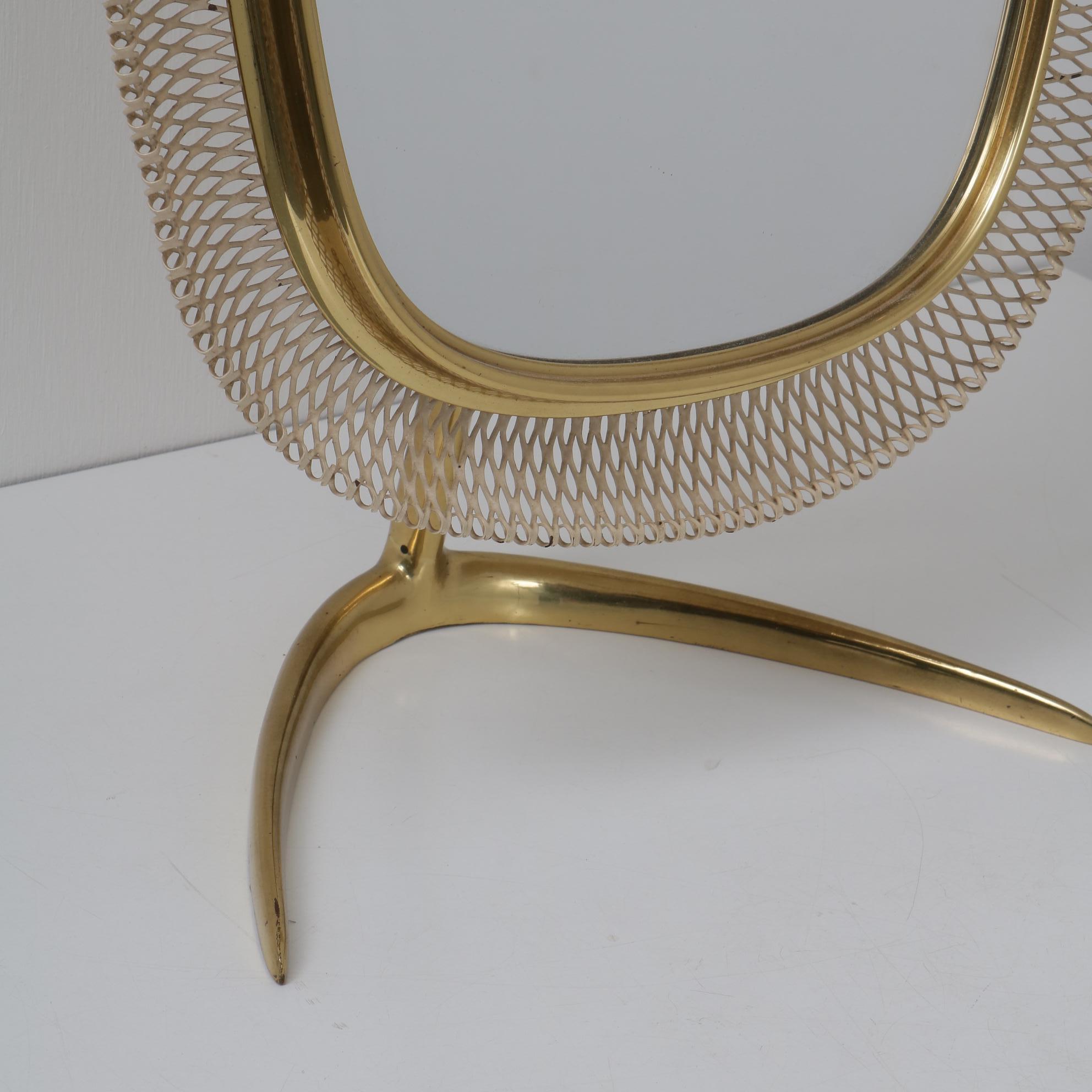 A beautiful vanity mirror, manufactured by Vereinigte Werkstätten München in Germany, circa 1950.

This quality piece is made of golden colored brass with a white perforated metal edge. It stands on a curved foot, the mirror itself has a